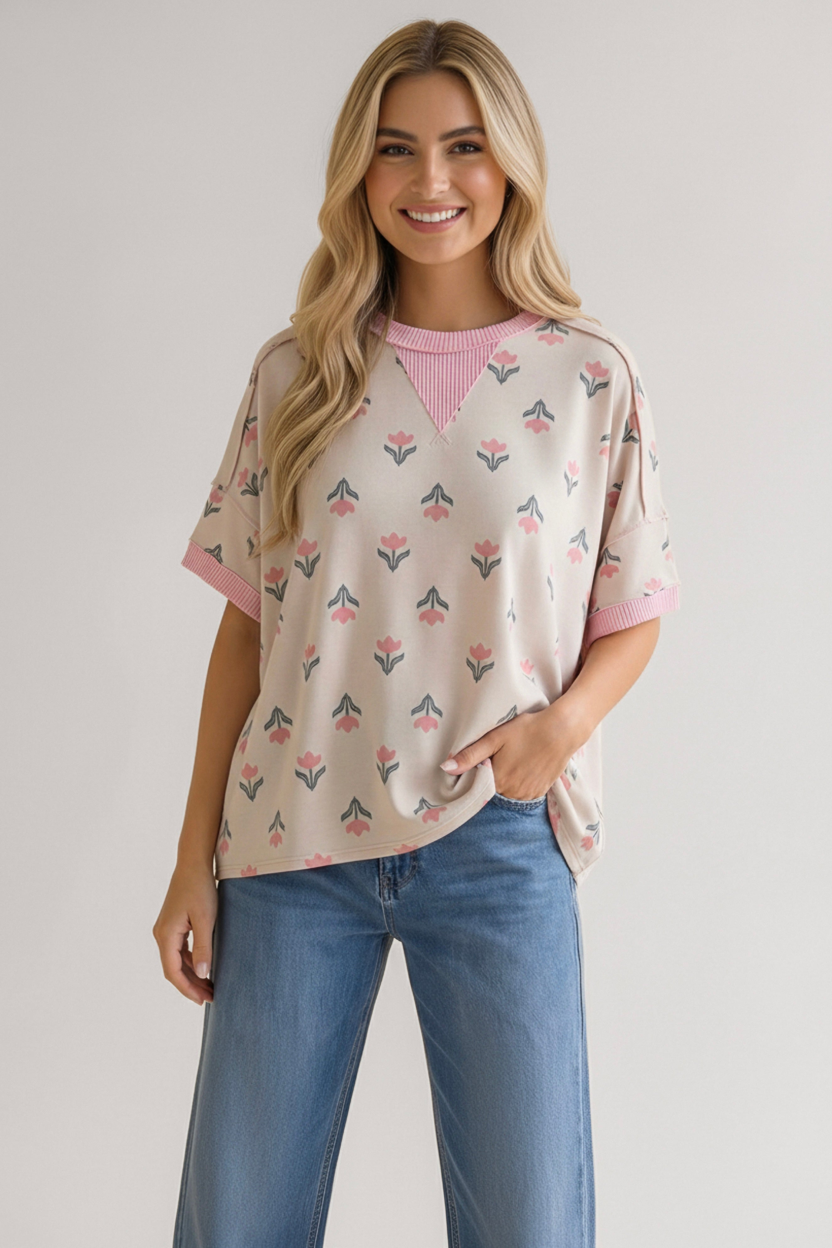 Smiling woman wearing relaxed cream tee with pink floral print and striped neckline paired with wide-leg blue jeans