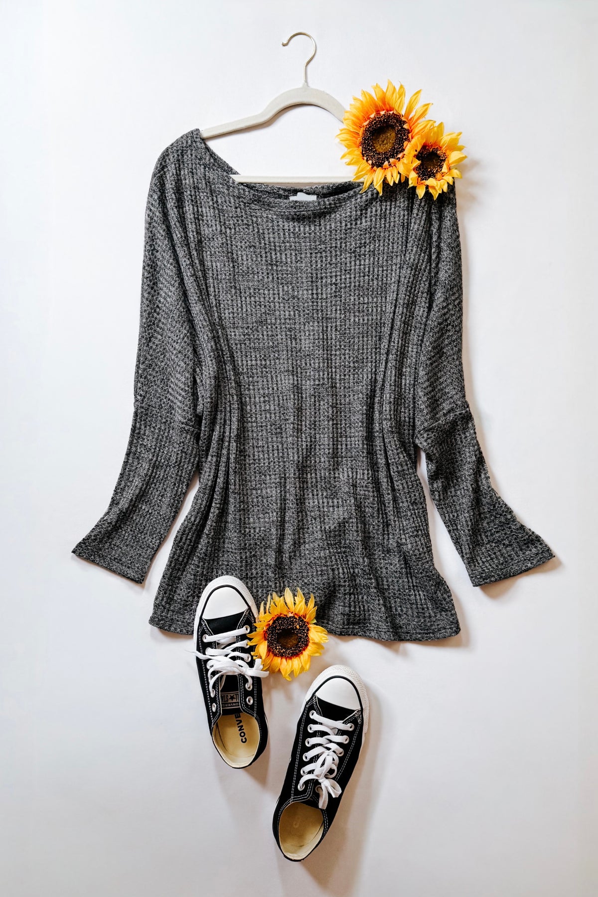 Charcoal ribbed boat neck top with relaxed dolman sleeves and flared cuffs displayed with sunflowers and black sneakers