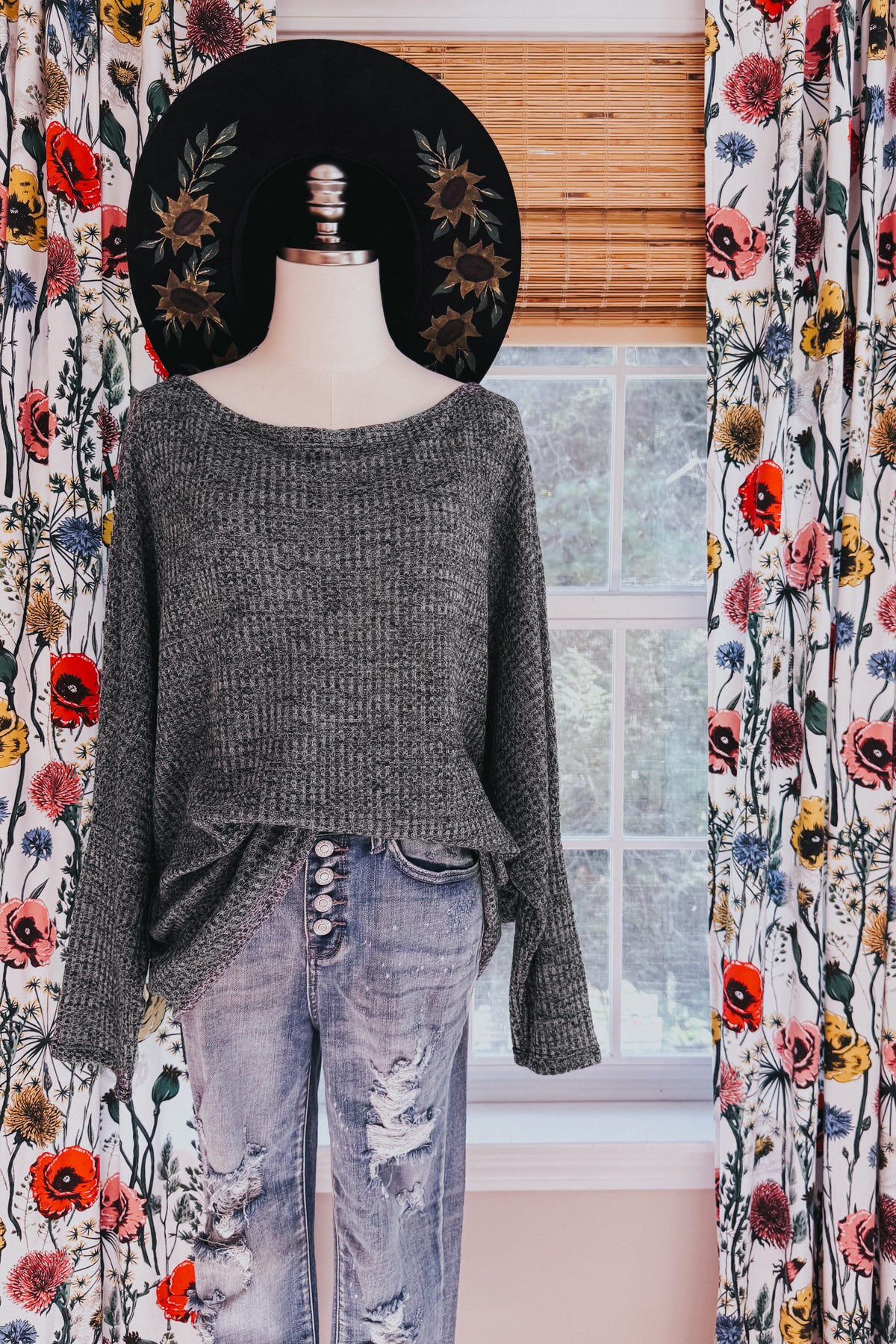 Charcoal ribbed boat neck top with relaxed dolman sleeves styled on a mannequin with distressed jeans and a floral black hat
