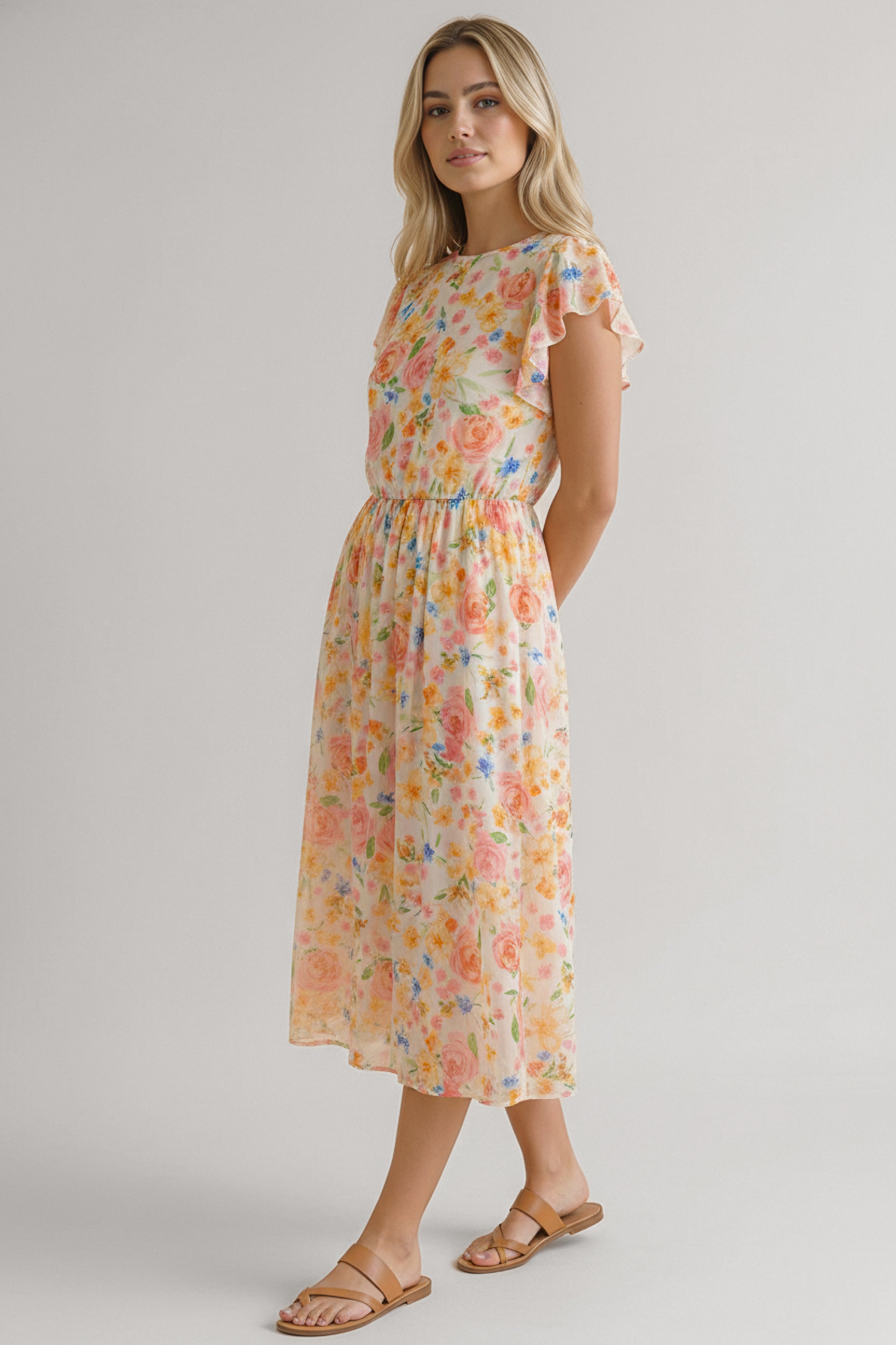 Blonde woman wearing a midi dress with soft orange floral print and flutter sleeves standing against a plain background