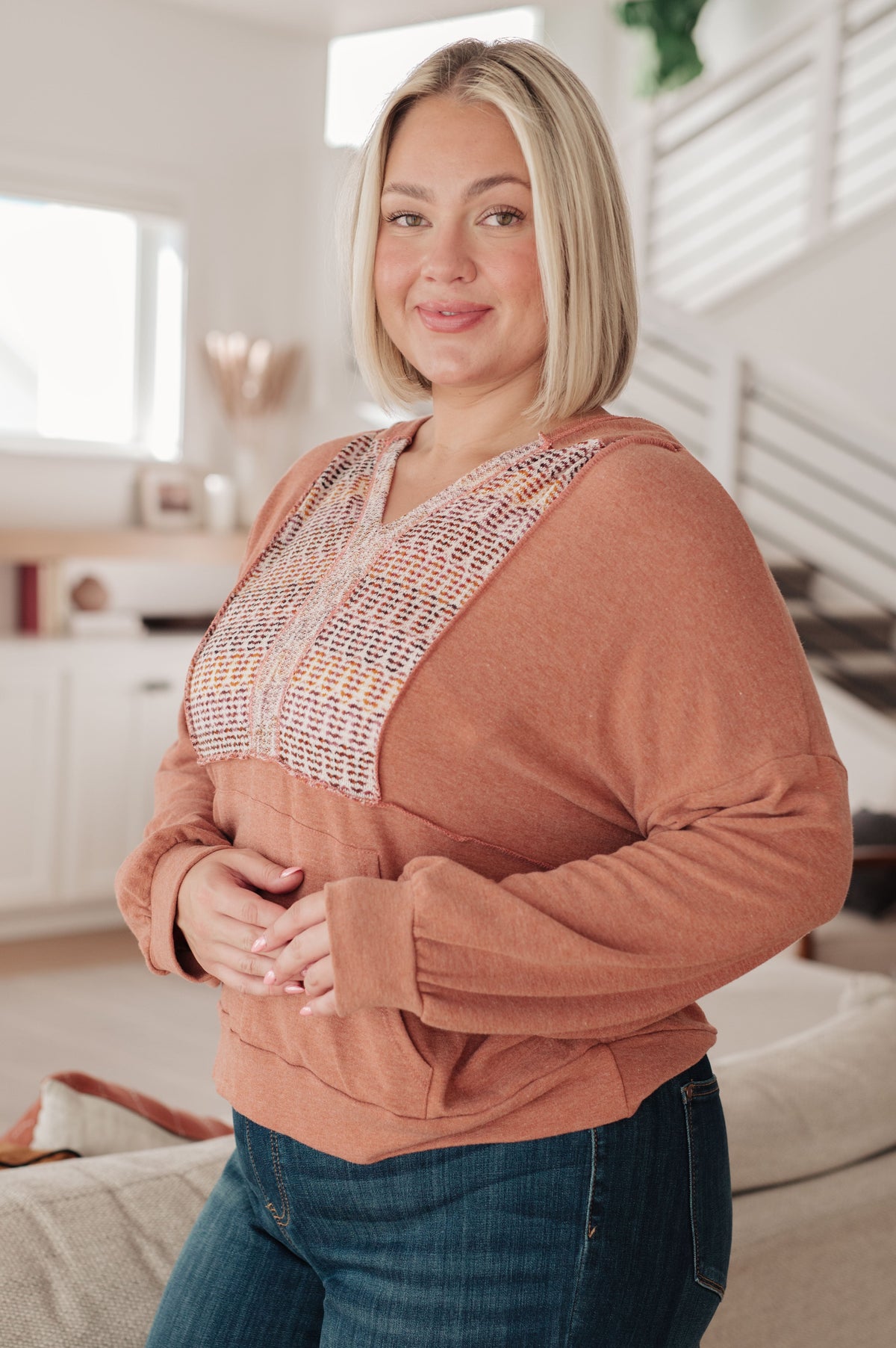 Woman modeling a rust hooded jersey top with a multicolored textured front panel and kangaroo pocket indoors