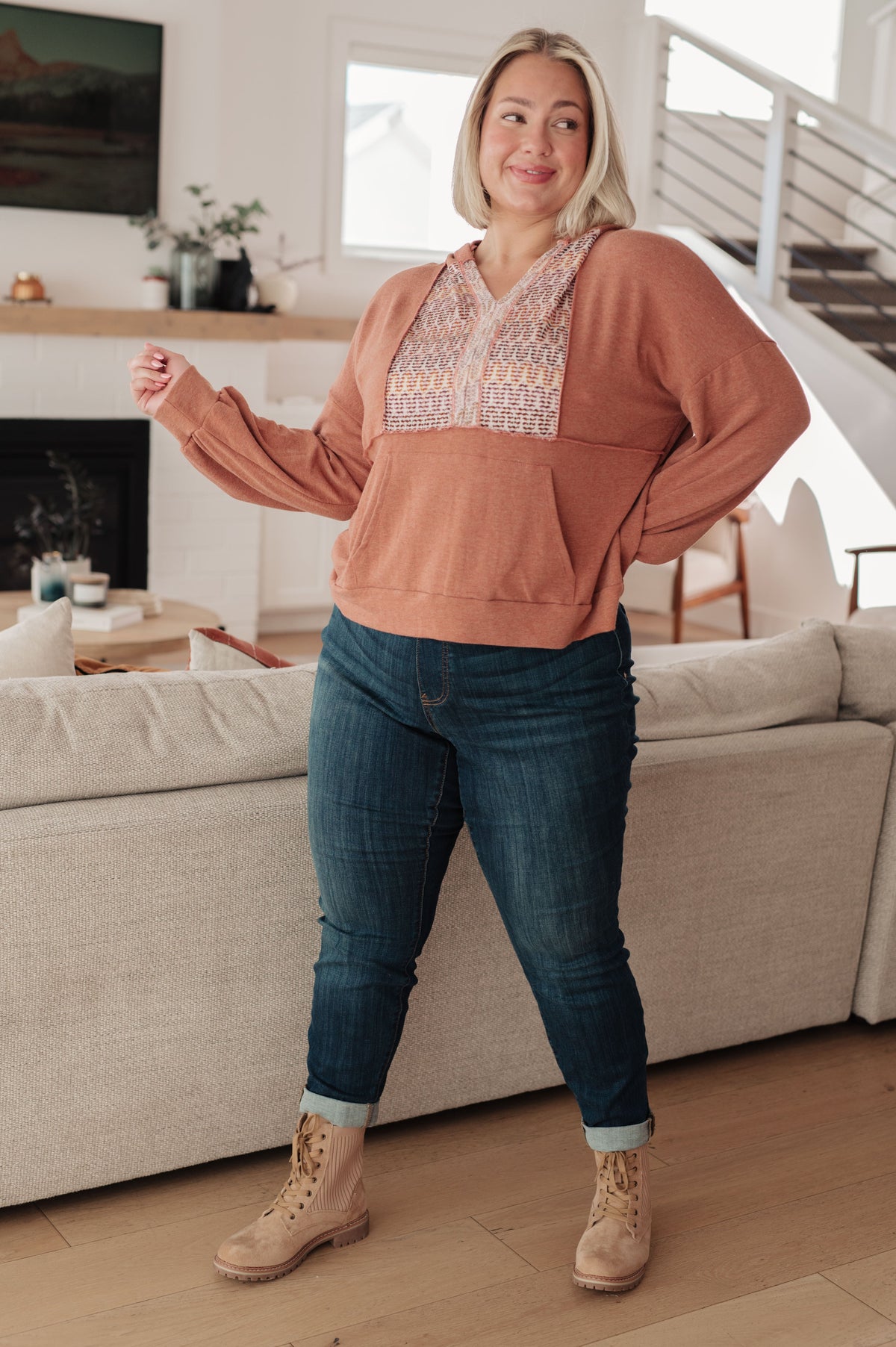 Woman modeling a rust hooded jersey top with a multicolored textured panel and jeans with tan lace up boots indoors