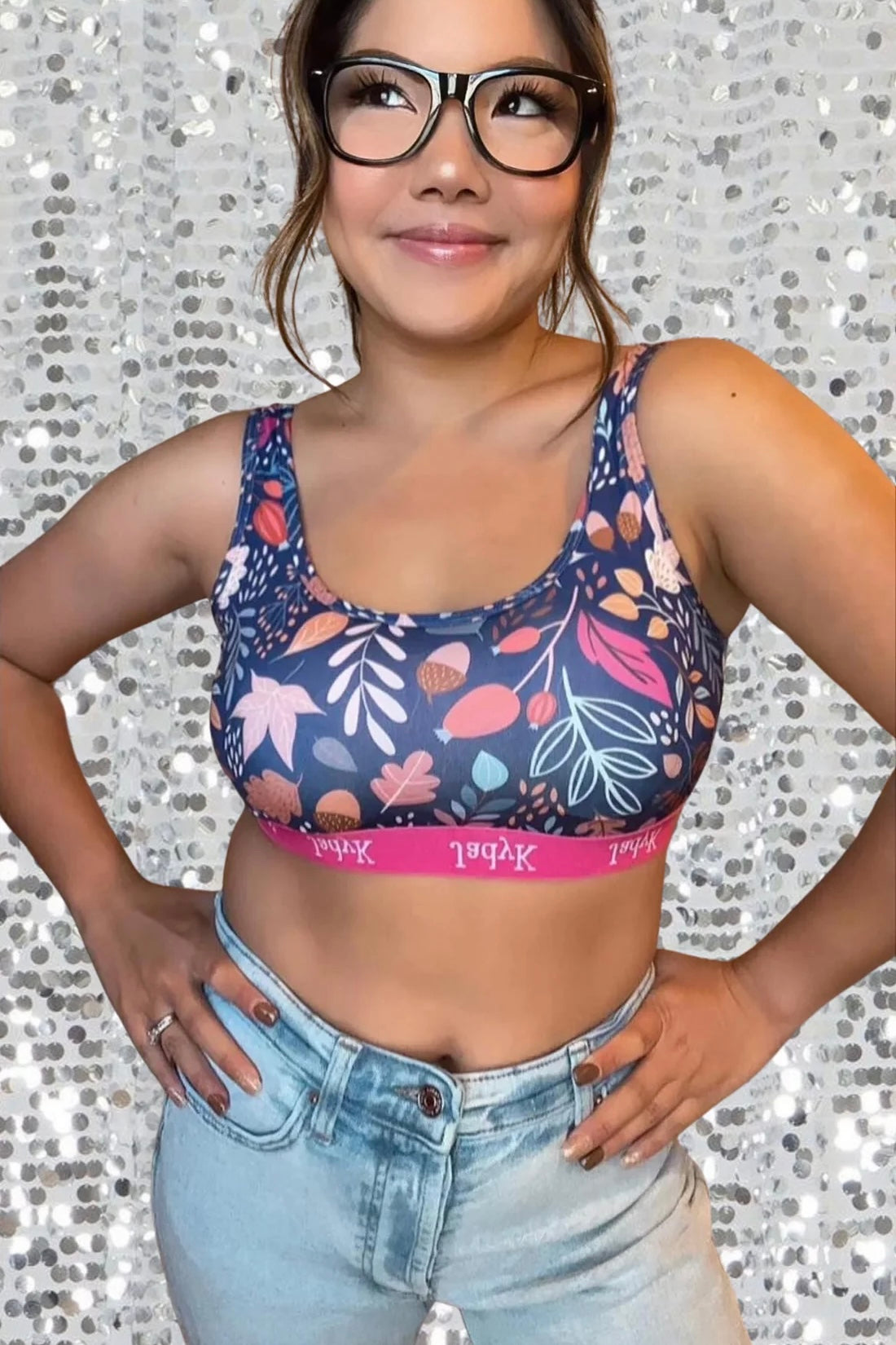 Woman wearing blue floral patterned bra with pink band and light wash jeans posing with hands on hips
