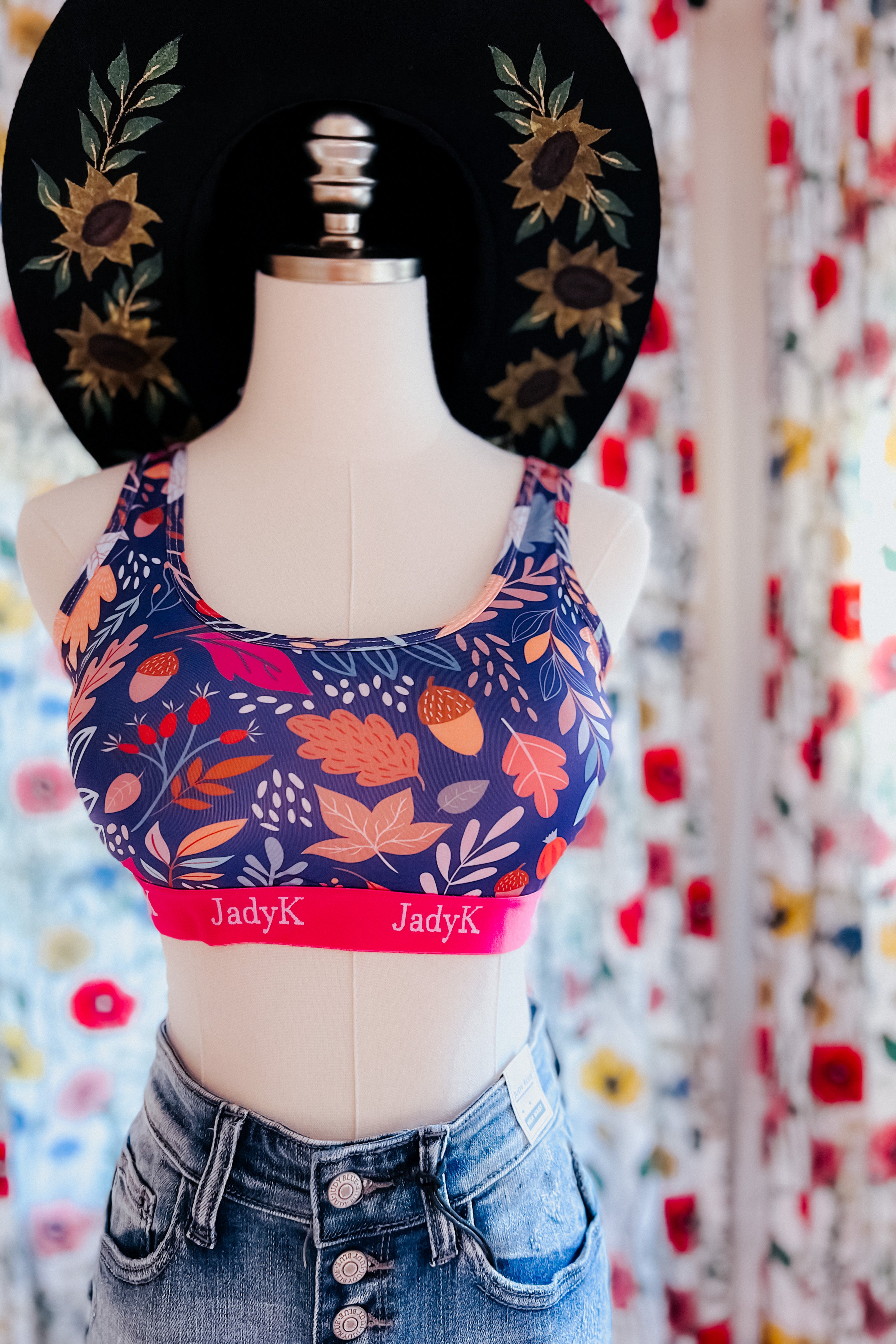 Blue sports bra with floral and leaf print, pink band, styled with high-waisted button-fly denim shorts and black embroidered hat
