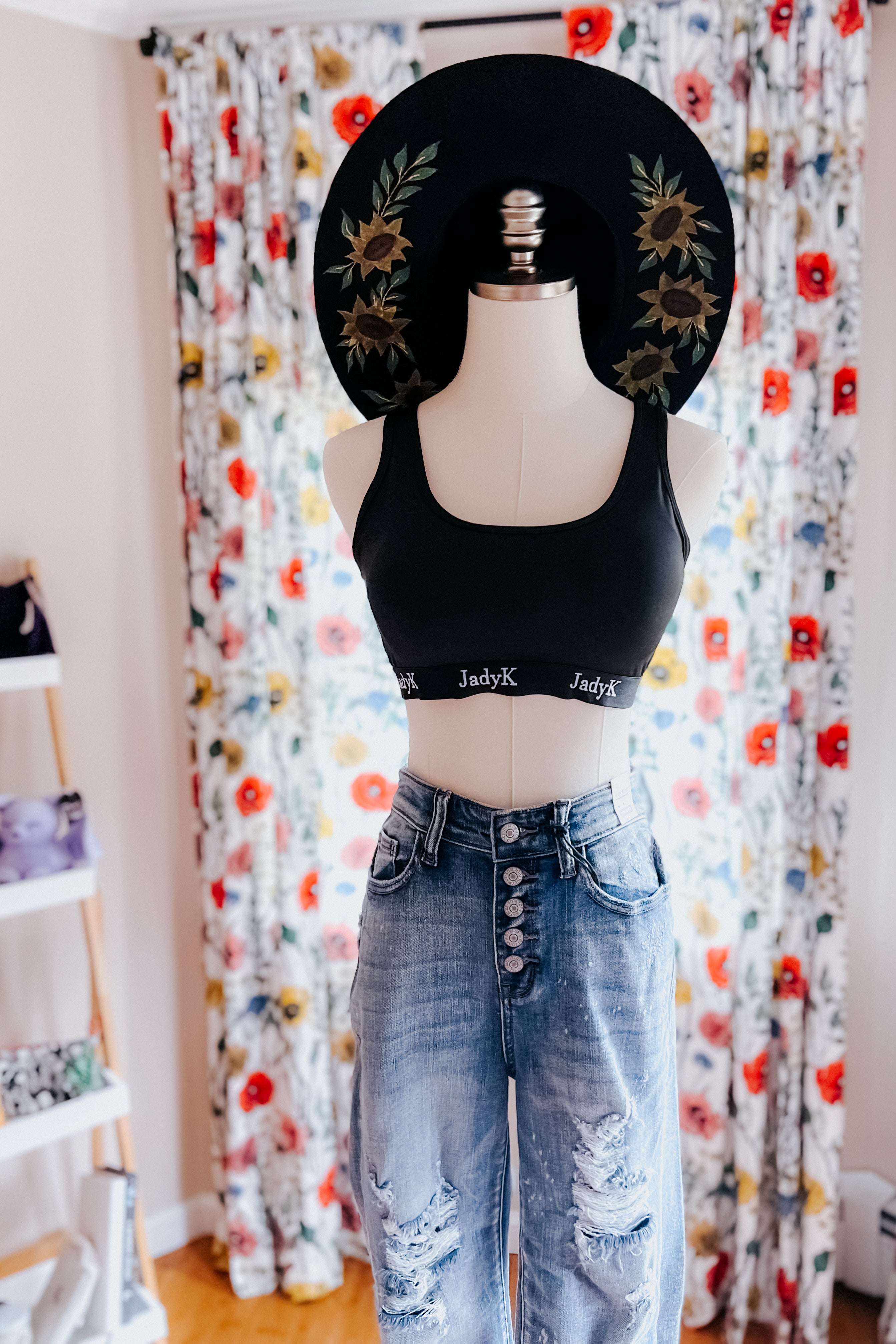 Black scoop bralette with logo band paired with high-waisted distressed denim jeans and sunflower-printed hat on mannequin