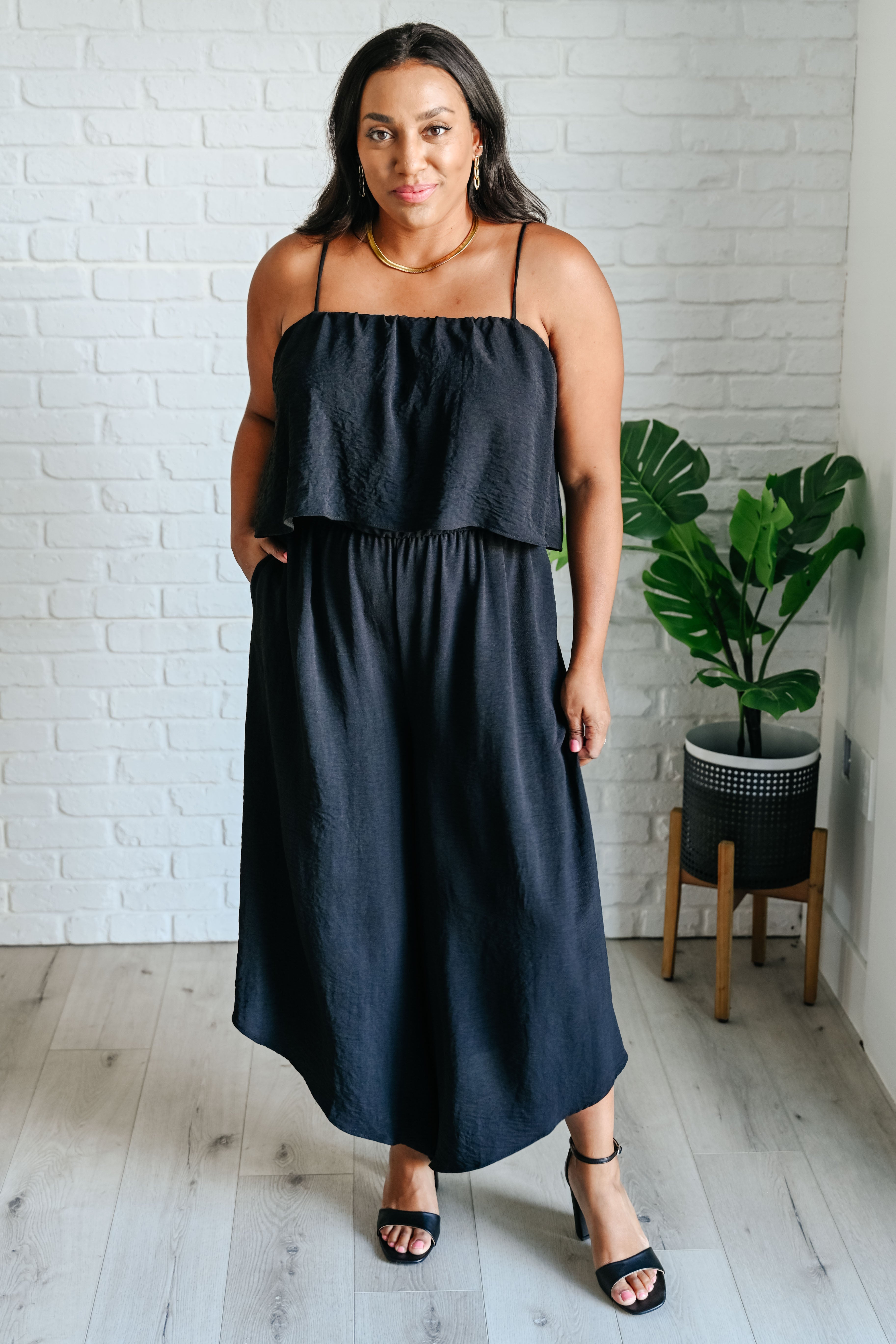 Woman wearing a black layered sleeveless midi dress with thin straps and side pockets standing indoors