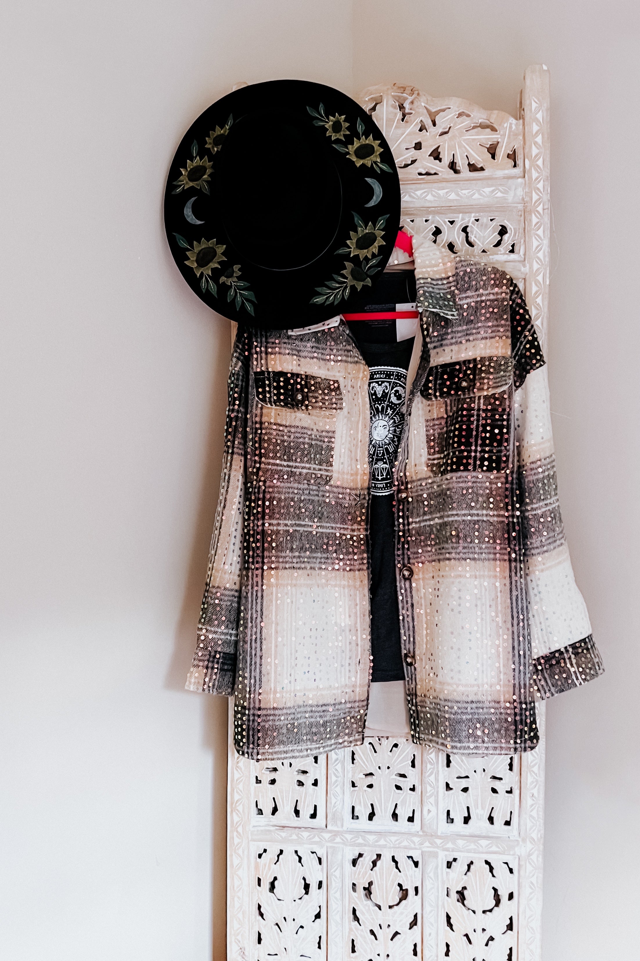 Beige and black plaid sequin shacket layered over graphic tee, paired with black hat decorated with sunflowers and crescent moons