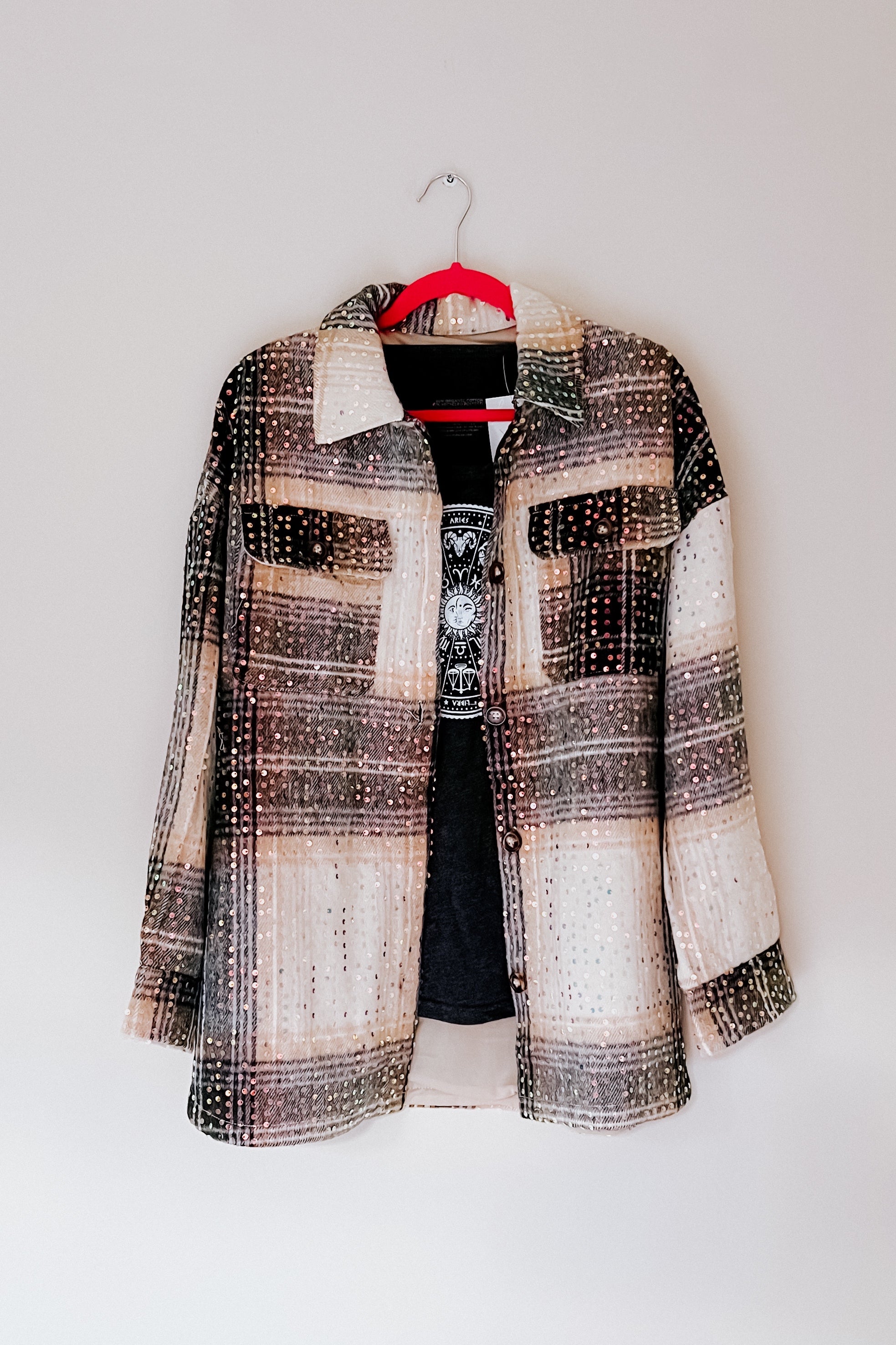 Beige and black plaid shacket with sequin embellishments hanging on red hanger against plain wall