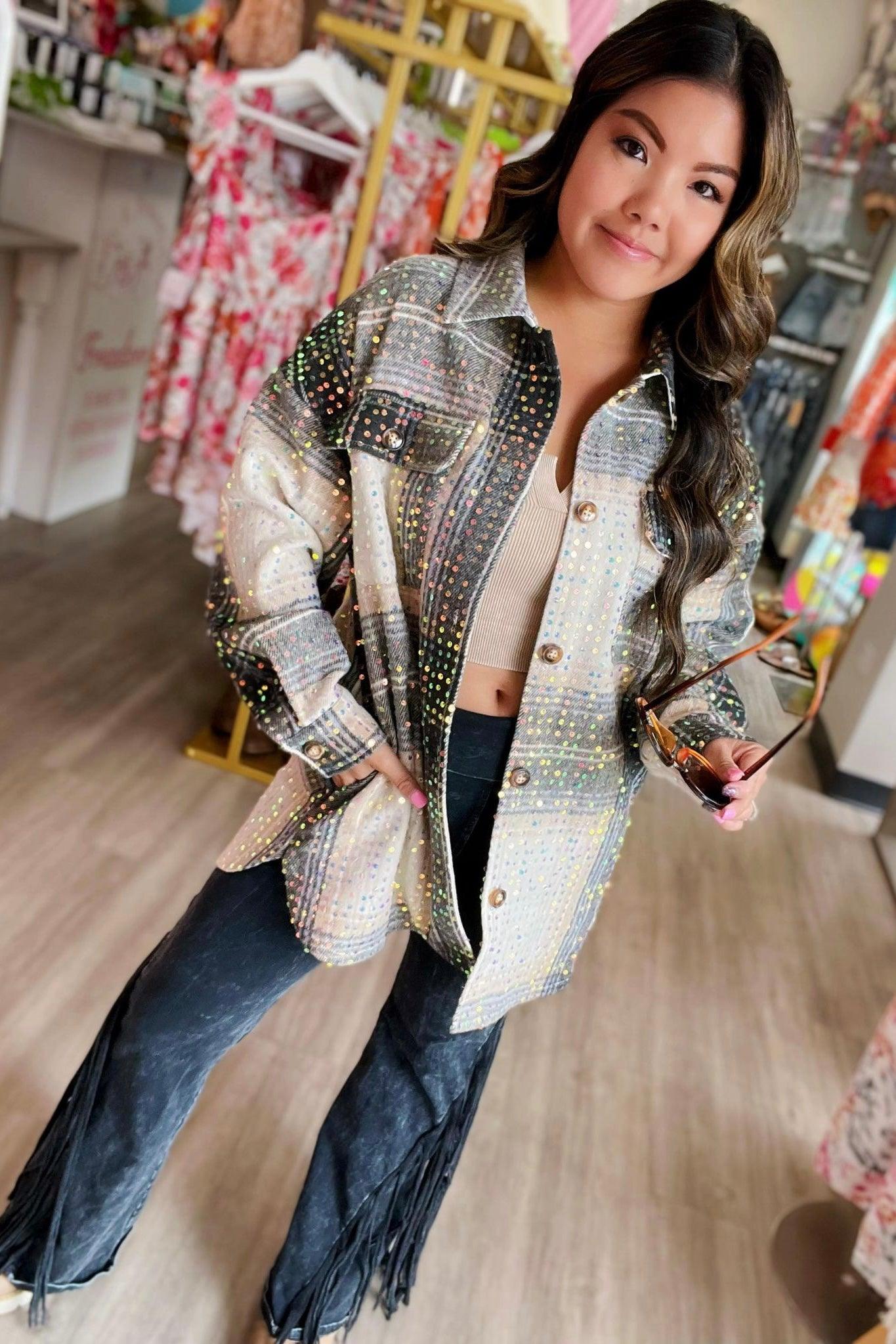 Woman wearing beige and black sequin plaid shacket with fringe pants, holding sunglasses in a bright boutique setting