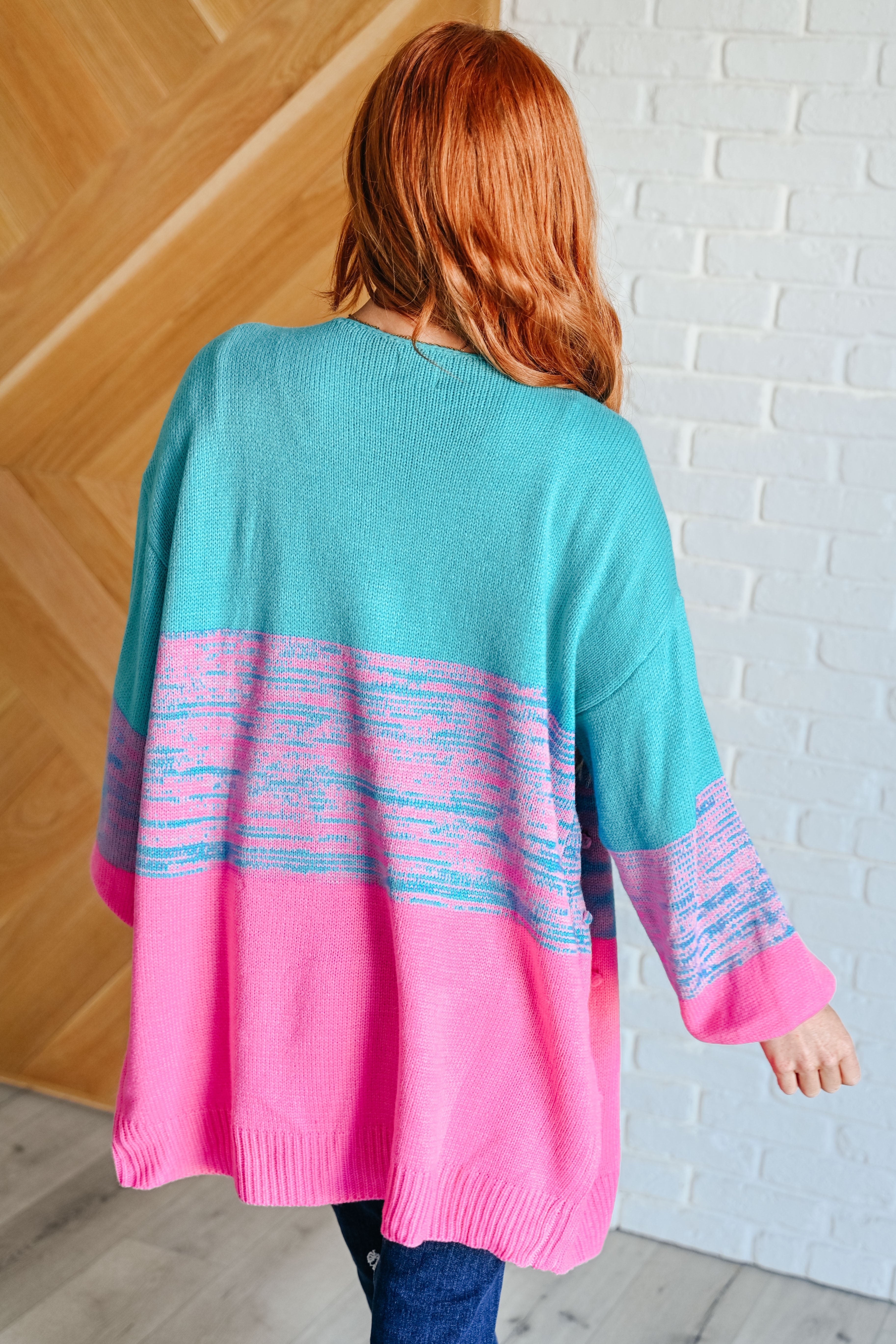 Woman wearing teal and pink open front cardigan with abstract pattern standing indoors facing away