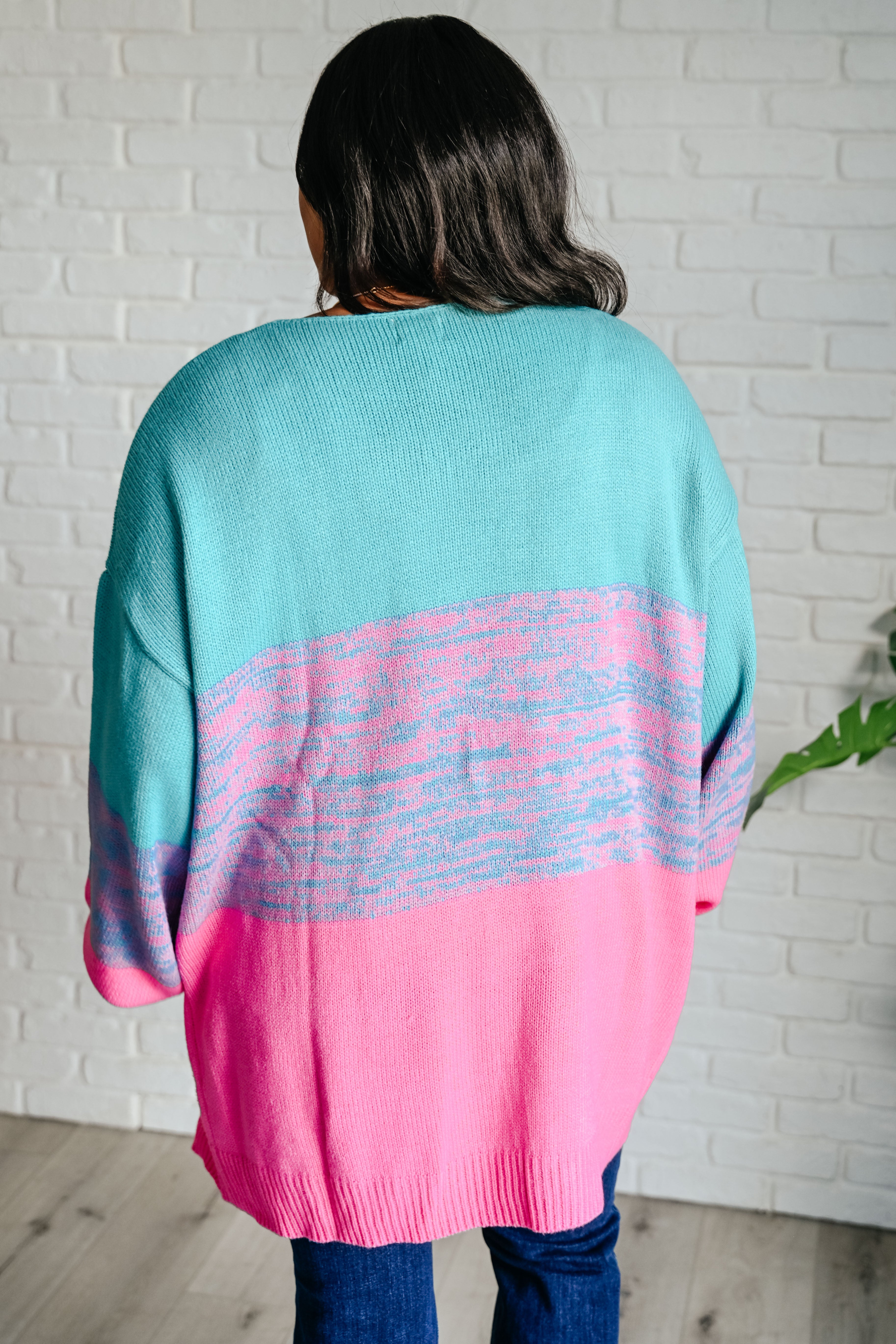 Woman wearing teal and pink color block cardigan with relaxed fit standing against white brick wall