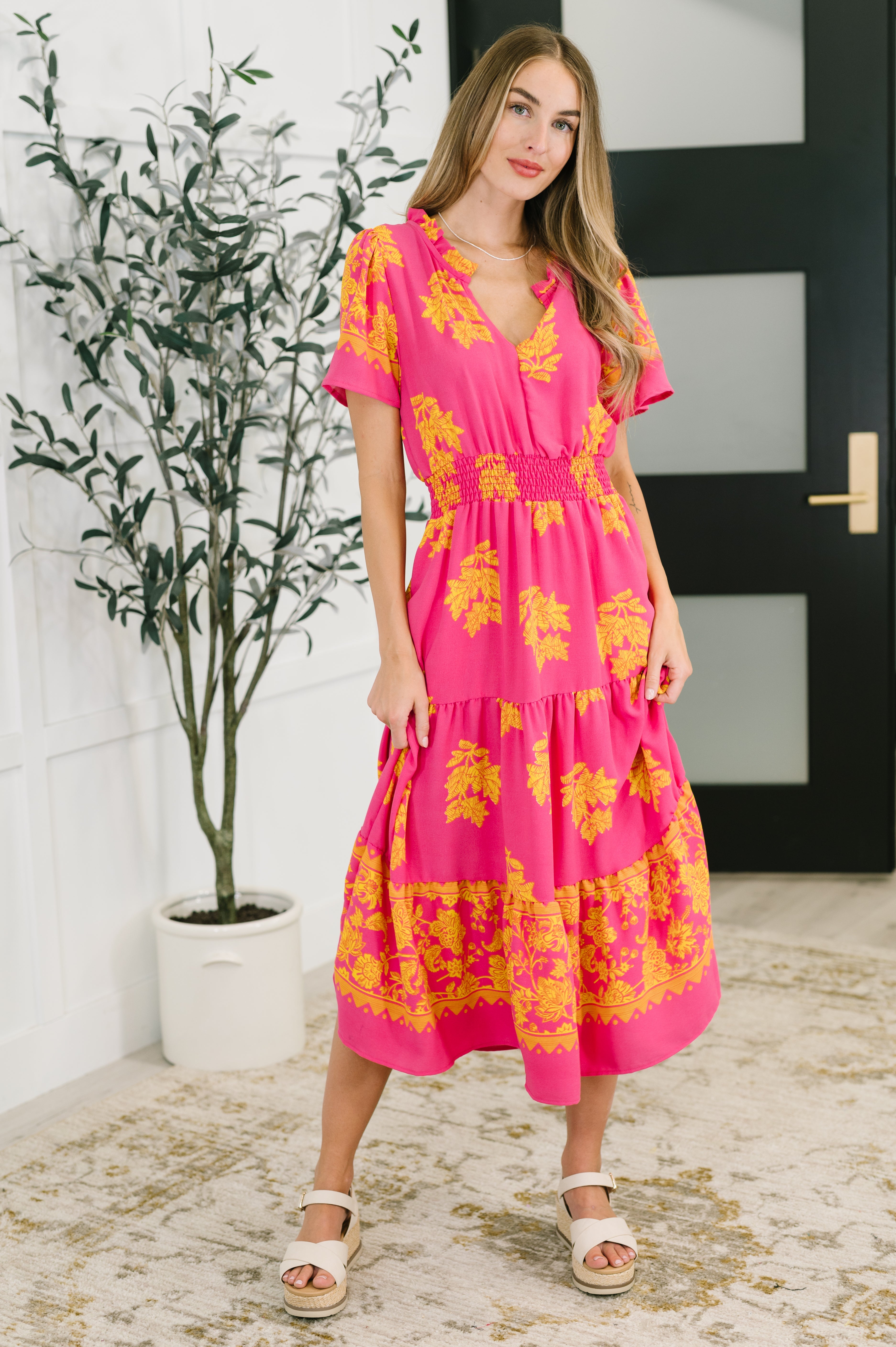 Woman posing indoors wearing a fuchsia midi dress with yellow floral print and smocked waist detail