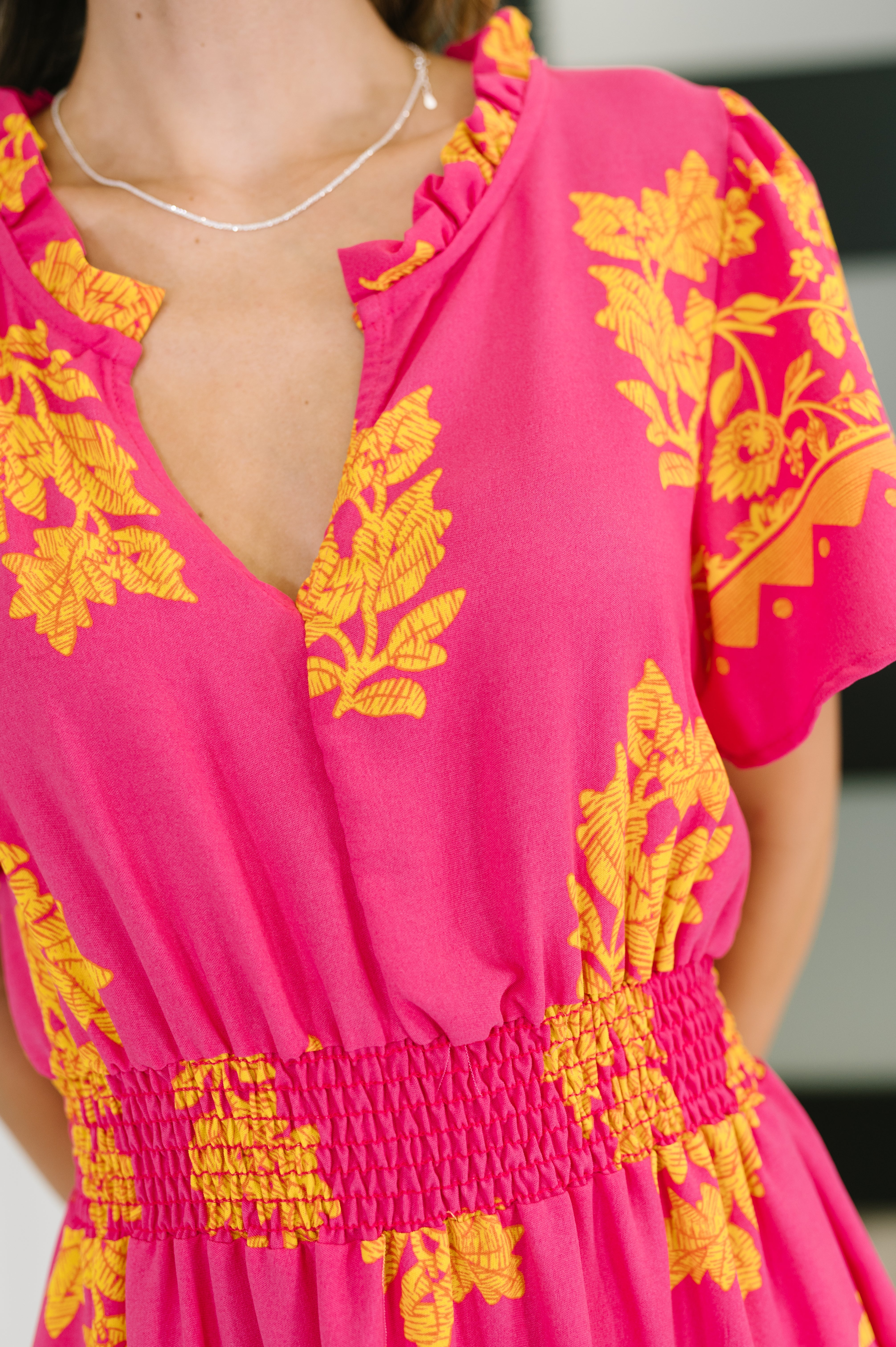 Close-up of fuchsia V-neck dress with yellow floral print and smocked waist detail on short sleeves