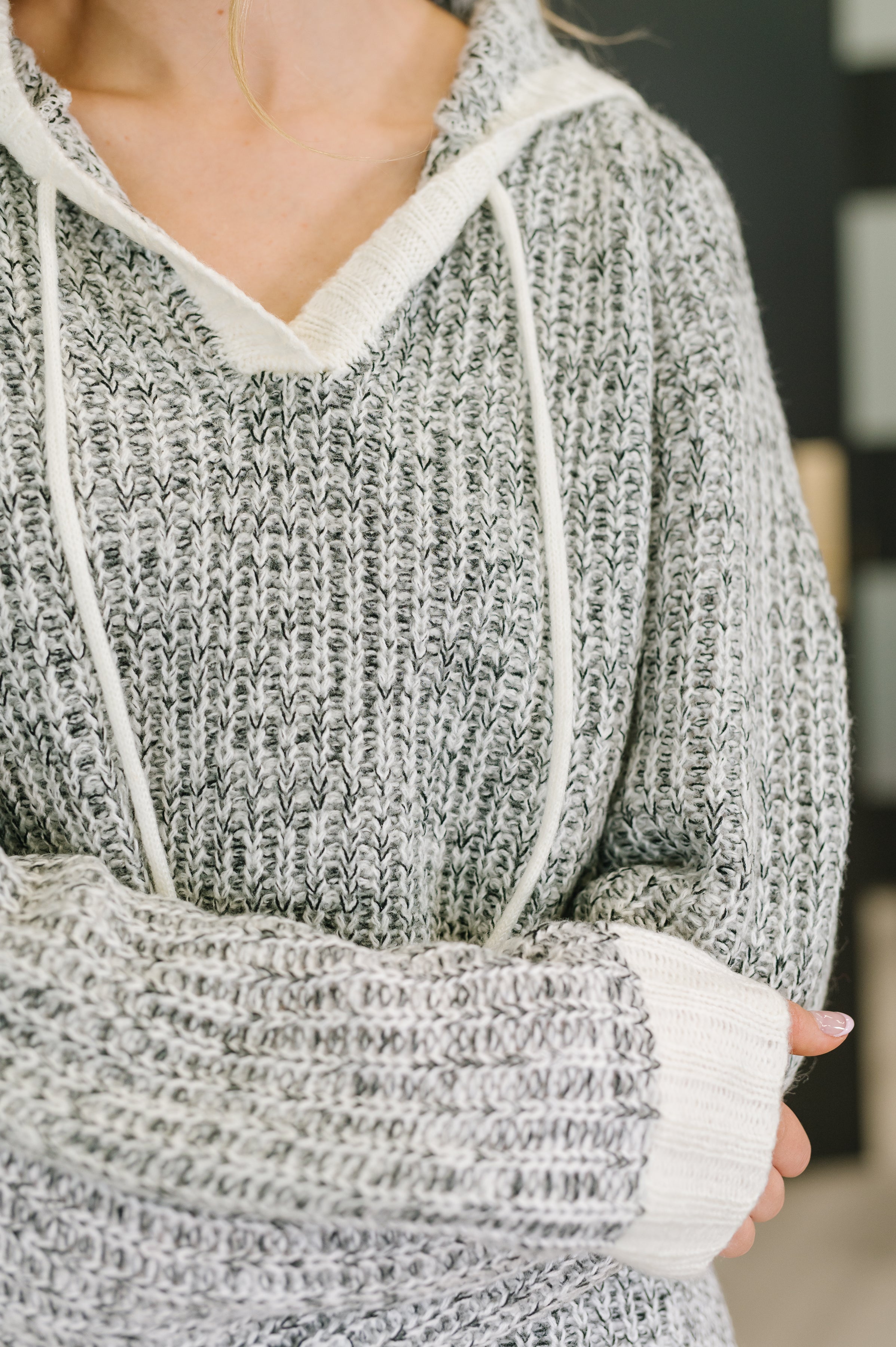 Close-up of grey textured knit pullover with split neck and white drawstrings worn by person indoors