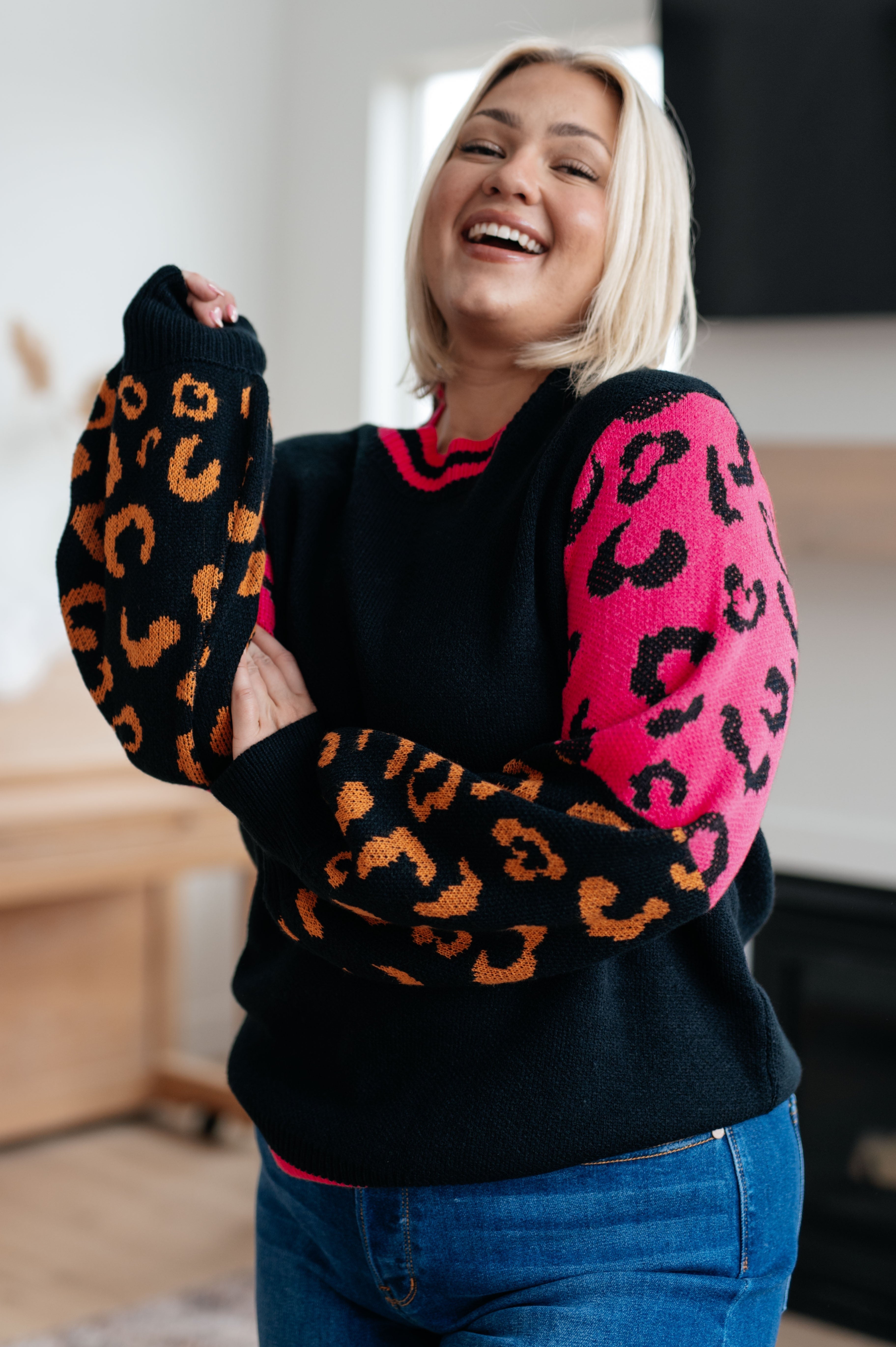 Woman wearing black sweater with bold orange and hot pink animal print sleeves, smiling indoors