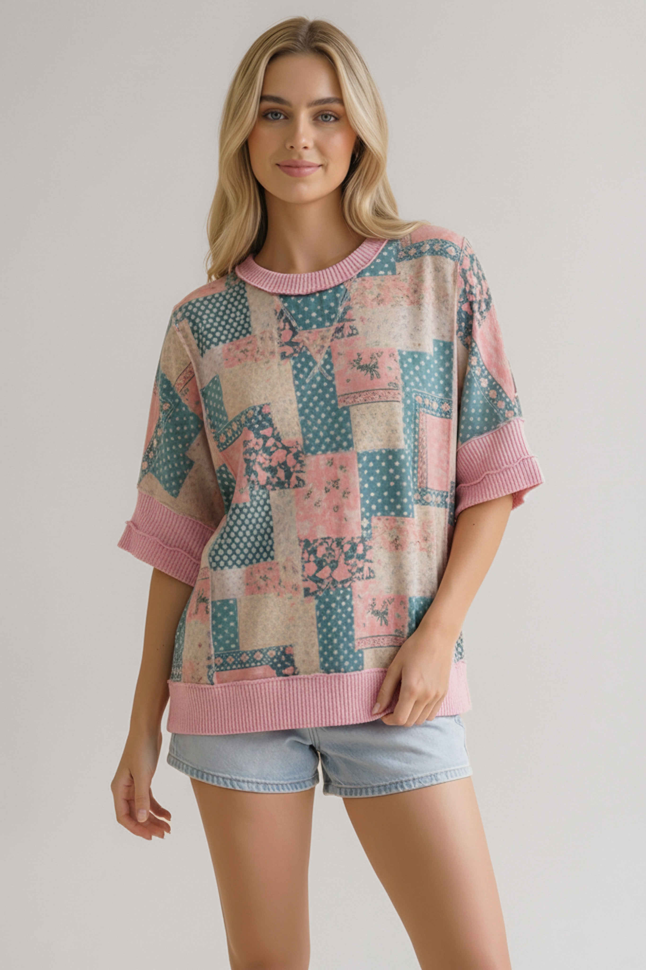 Woman wearing oversized short sleeve top with pink and teal patchwork pattern paired with light denim shorts