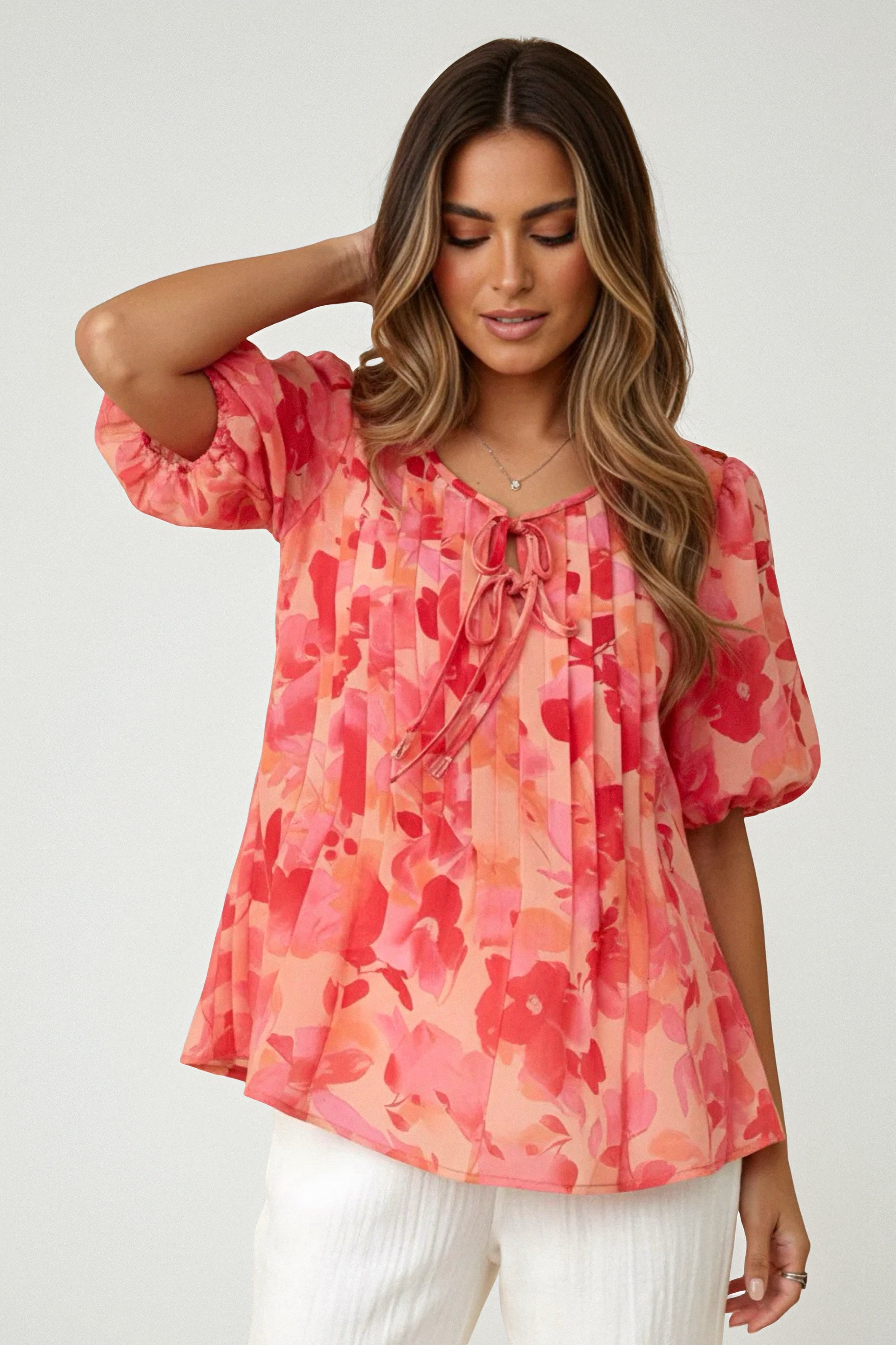 Woman wearing a peach blouse with vibrant floral print, puff sleeves, and tie detail paired with white pants