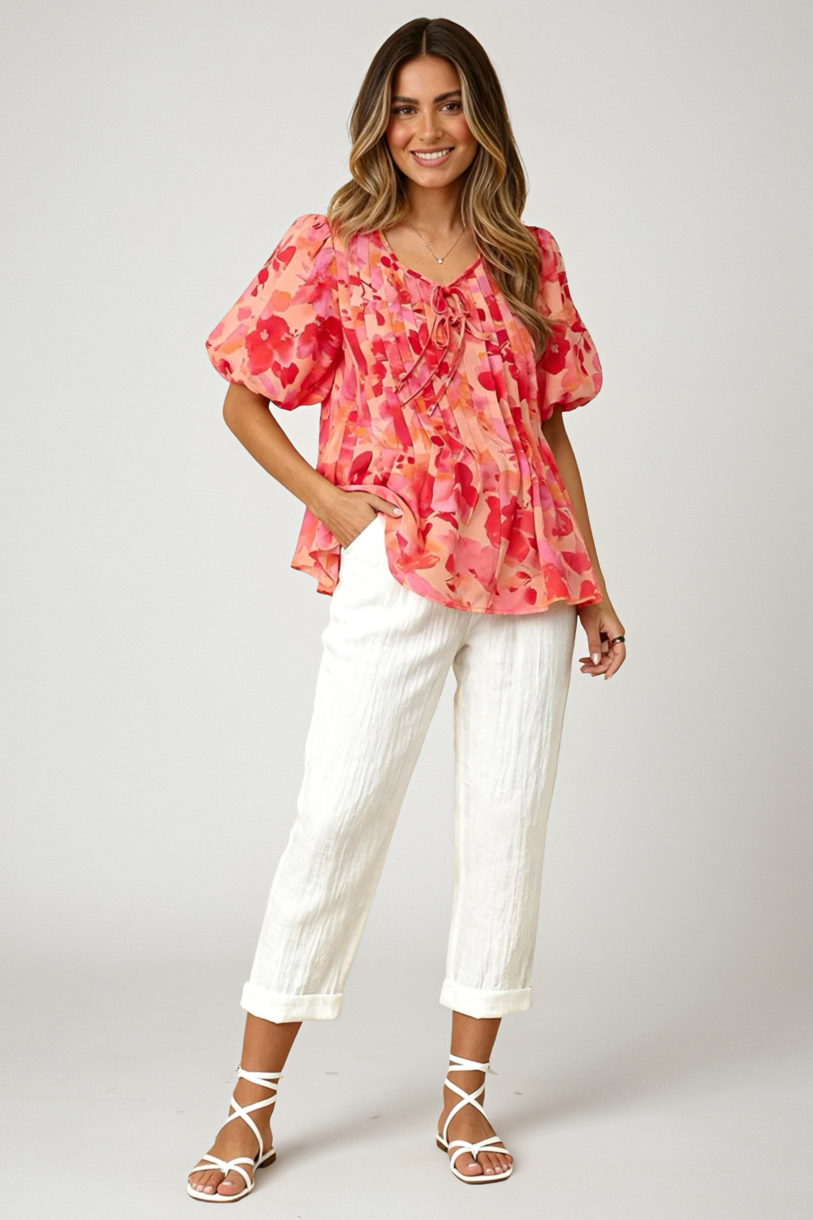 Smiling woman wearing a peach blouse with bright floral print and puff sleeves paired with rolled-up white pants and sandals