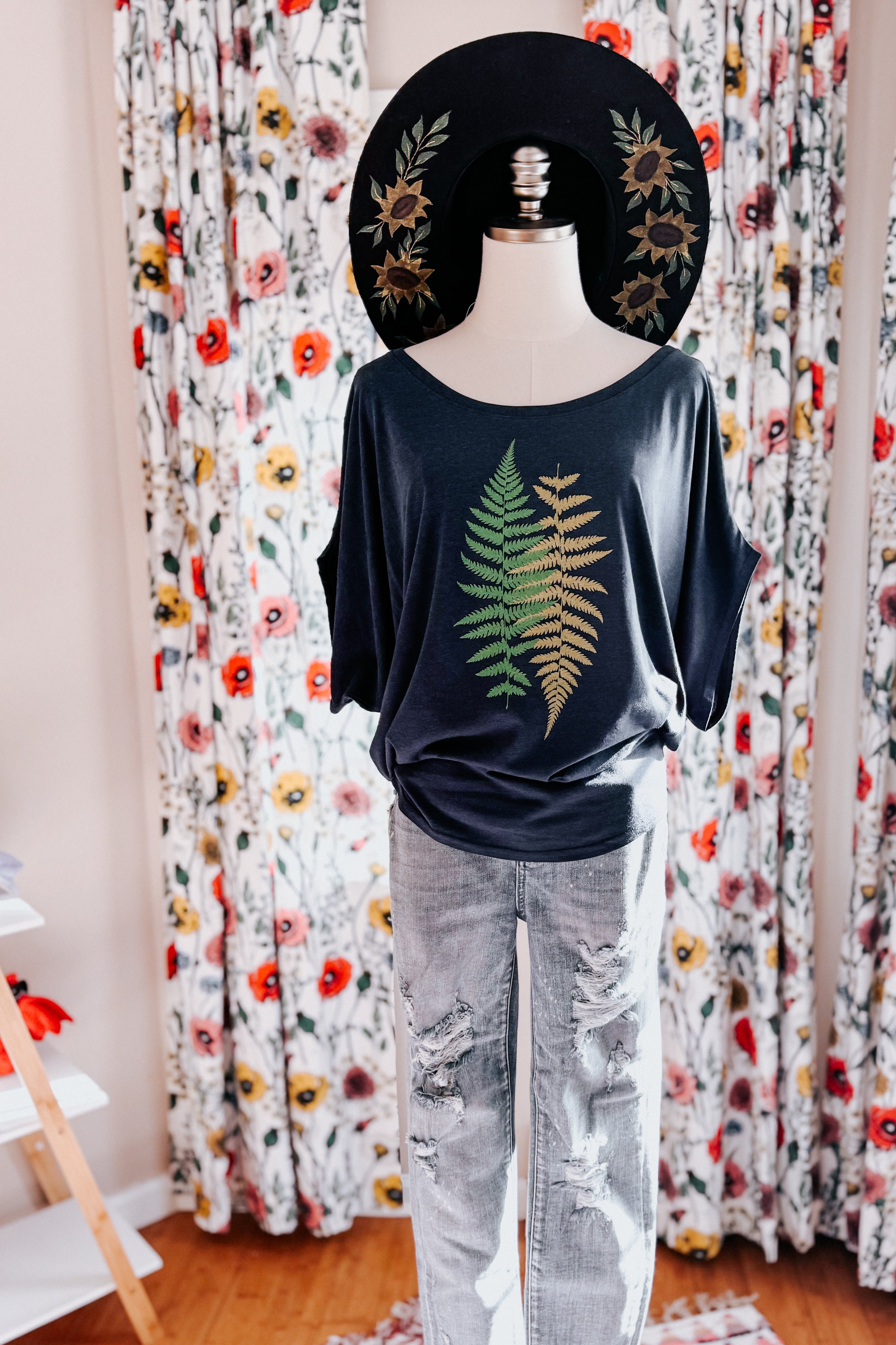 Navy bamboo dolman top with green and yellow fern print styled with distressed light-wash jeans and floral wide-brimmed hat