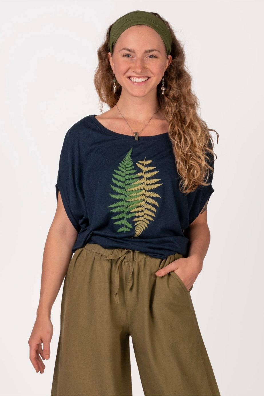 Smiling woman wearing navy bamboo dolman top with green fern print paired with olive wide-leg pants and headband