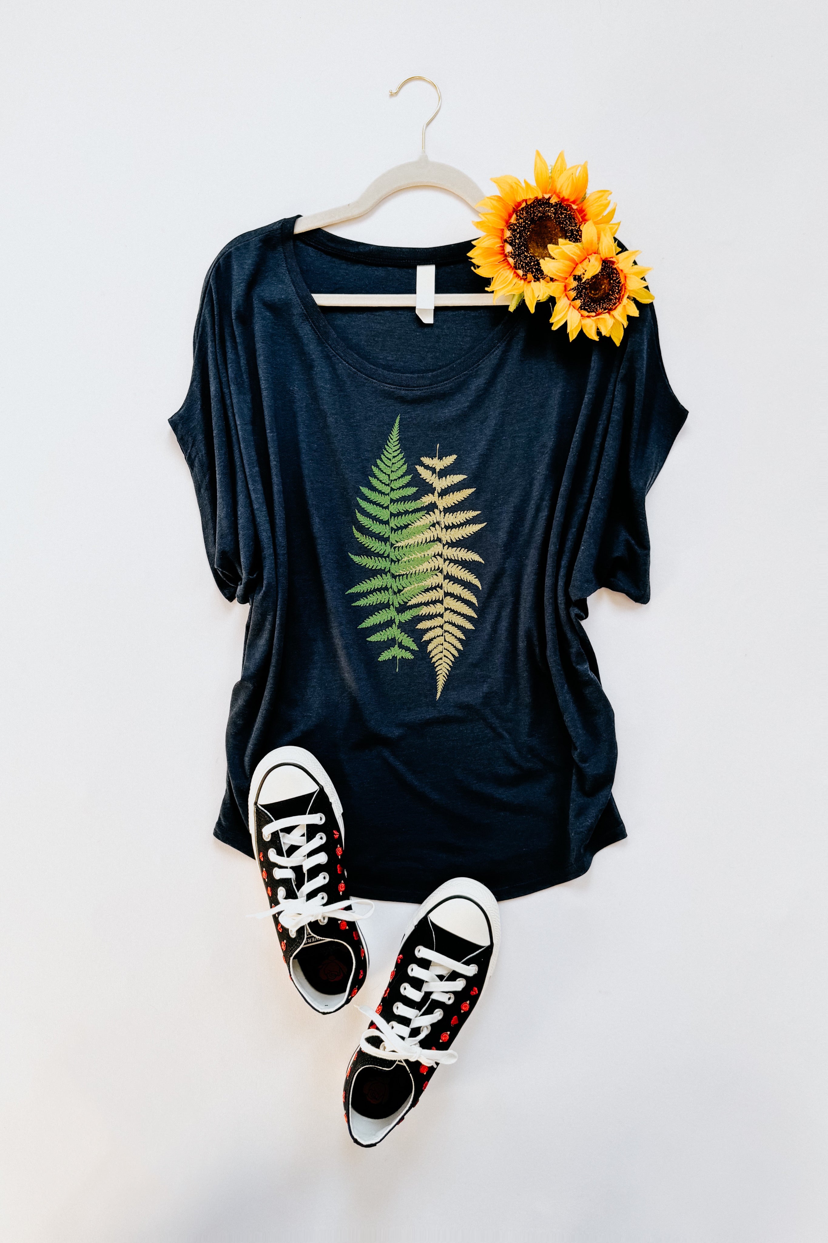 Navy bamboo top with green fern print styled with black floral sneakers and bright yellow sunflowers on hanger