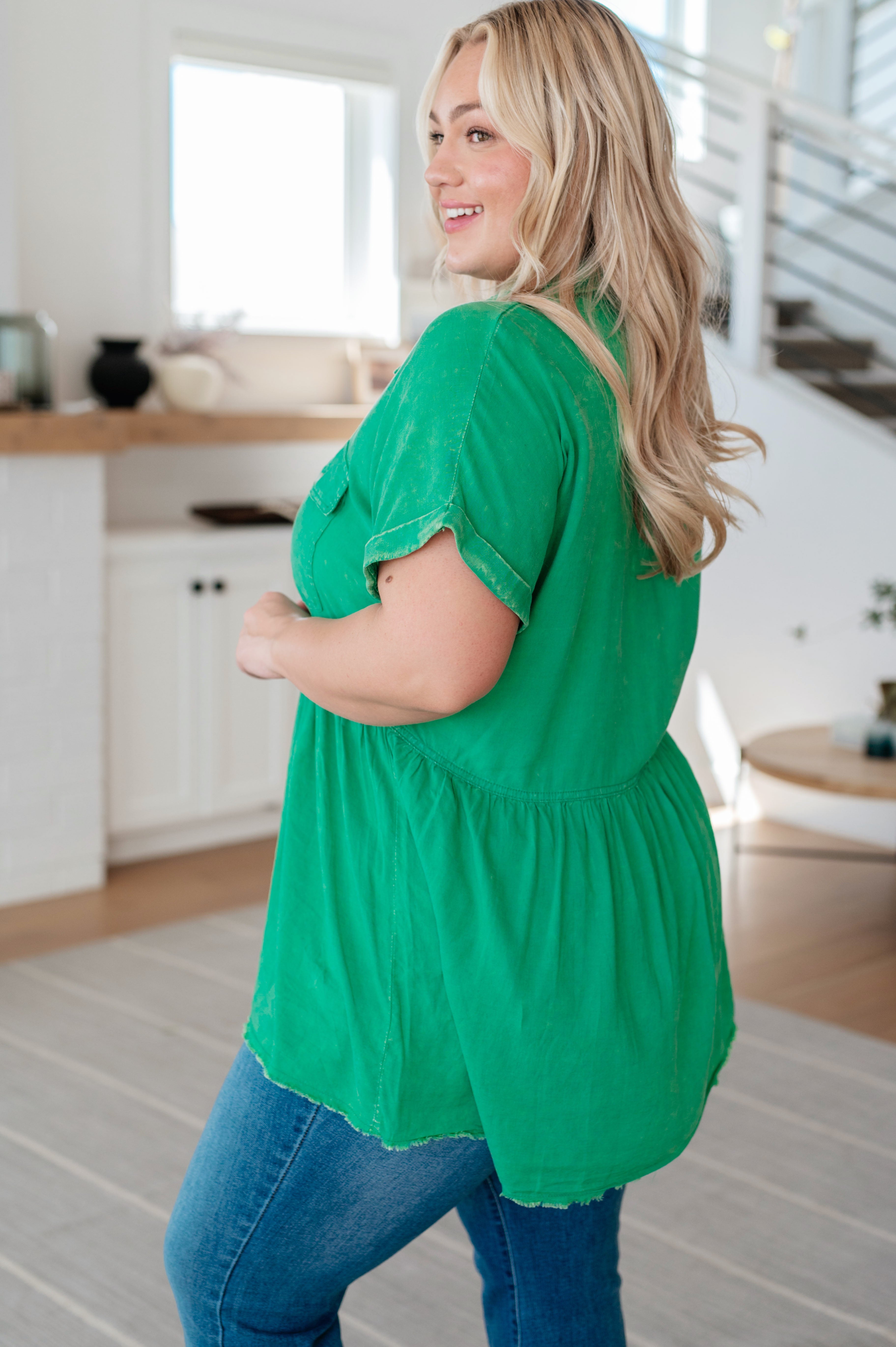 Curvy woman wearing vibrant green peplum blouse paired with blue jeans in bright, cozy home setting