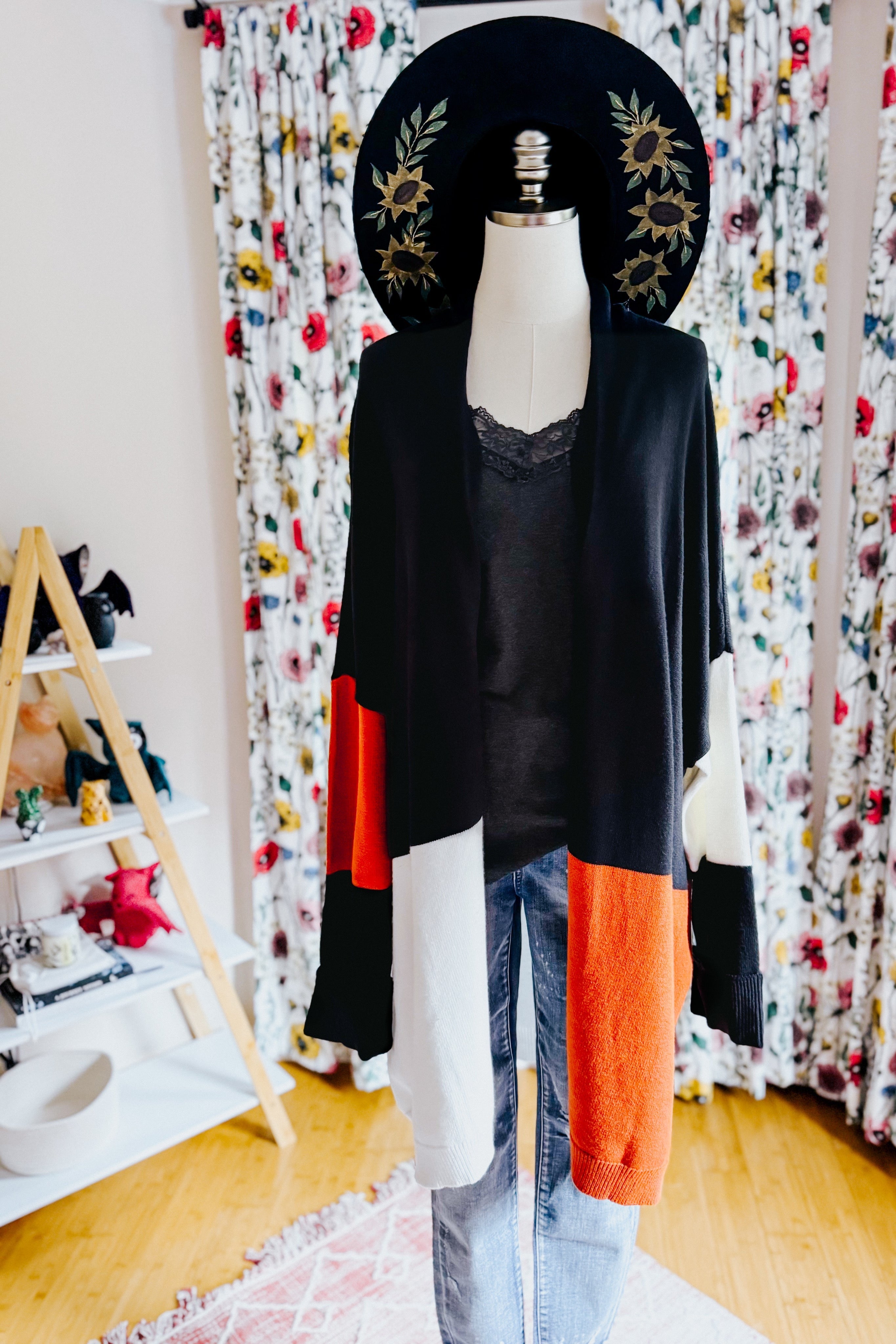 Black color block open-front cardigan styled with lace-trimmed black top and faded blue jeans on mannequin indoors