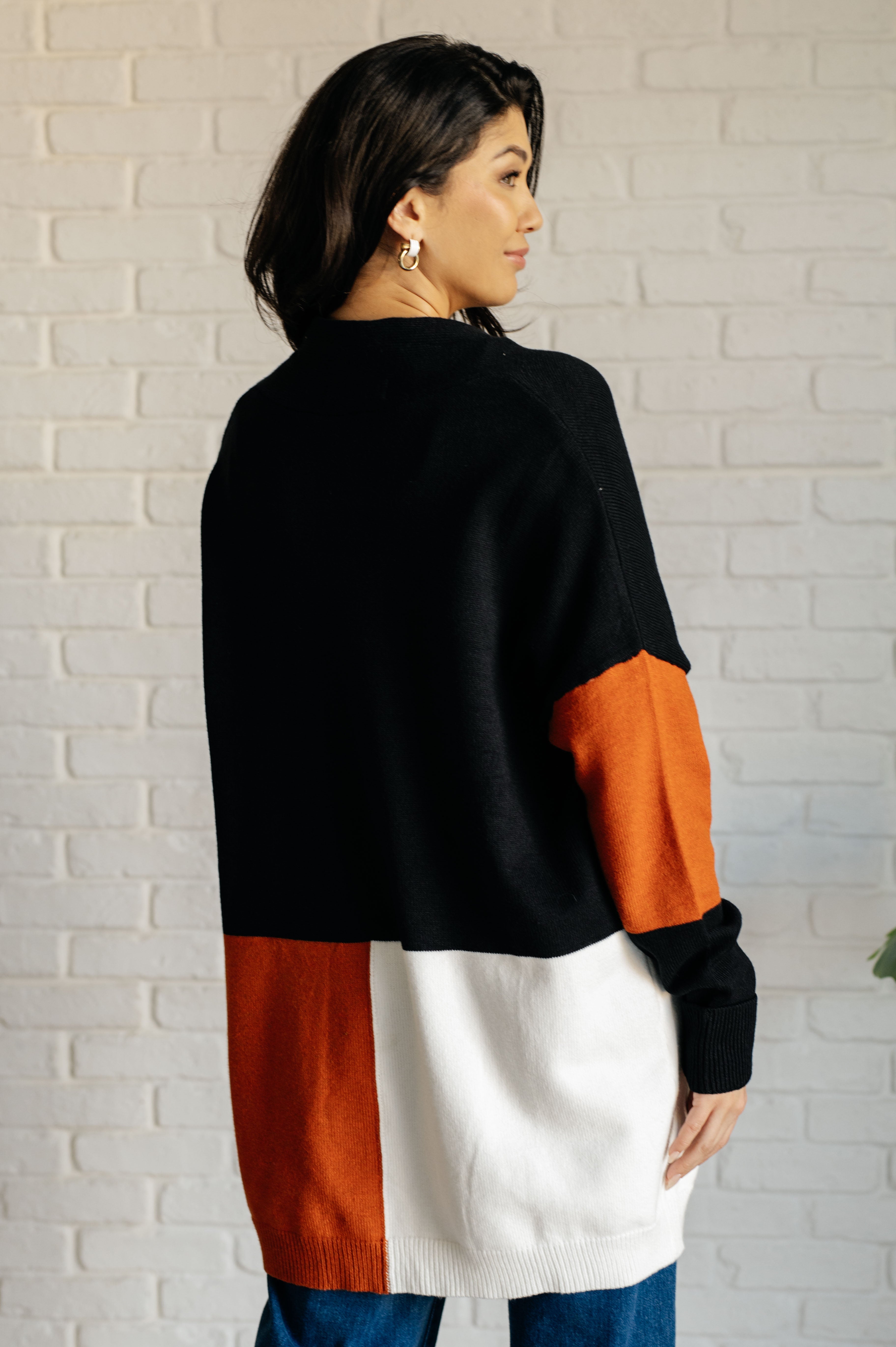 Woman wearing black, white, and rust color block cardigan with relaxed fit standing against white brick wall