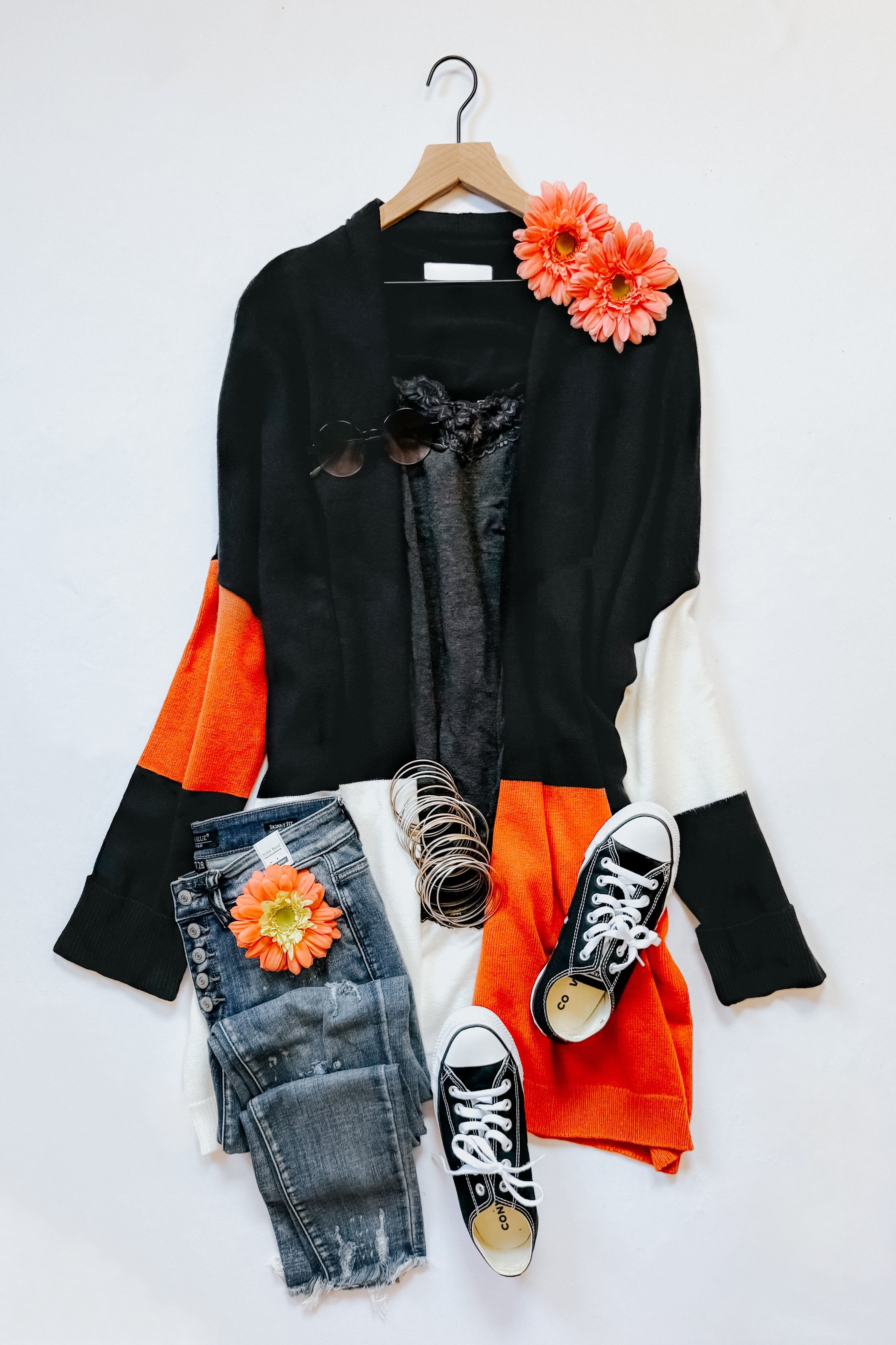 Black, orange, and white color block open front cardigan styled with distressed jeans, sneakers, and floral accents laid flat