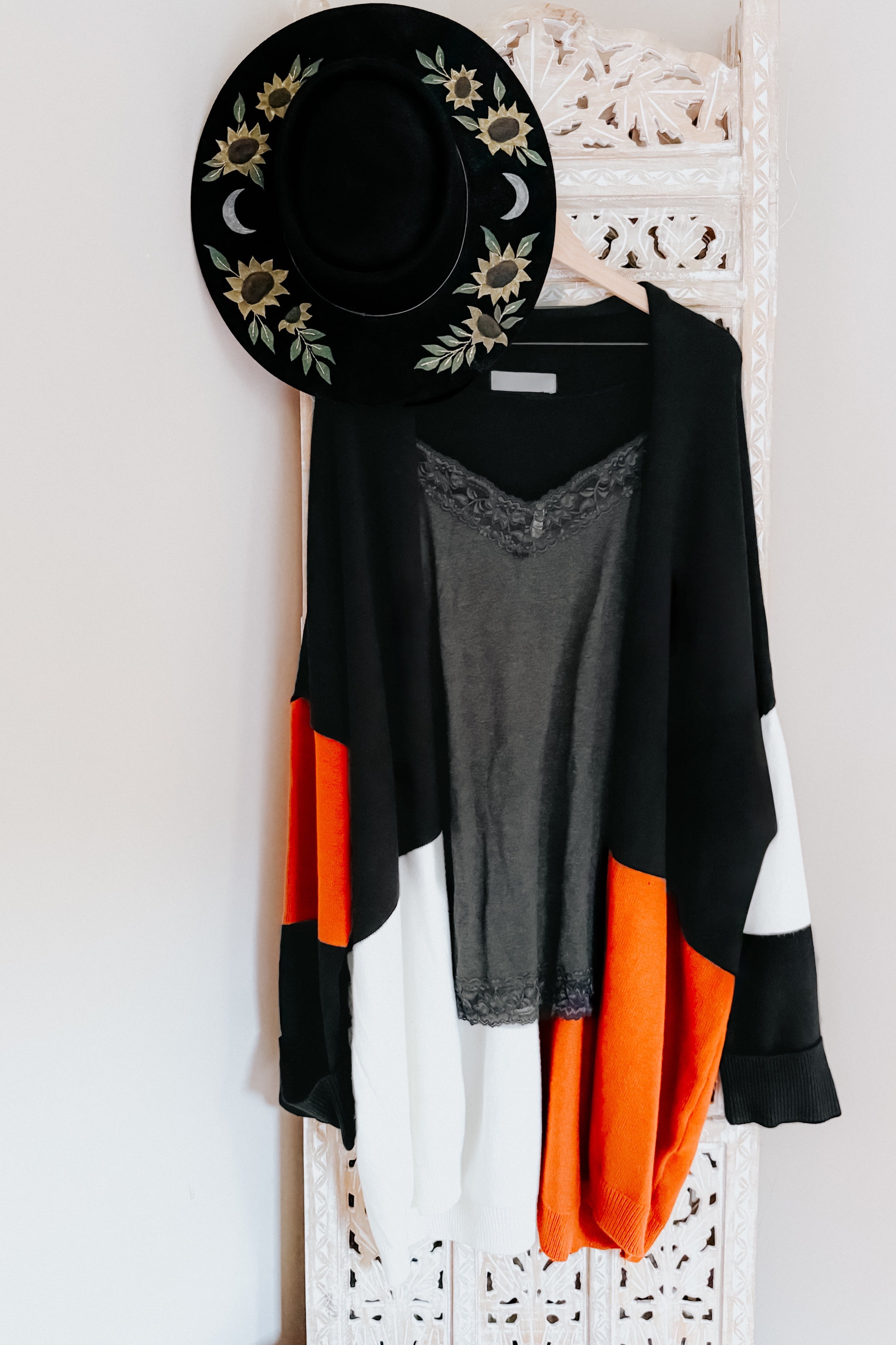 Black, white, and orange color block cardigan layered over gray lace-trim tank top with black floral embroidered hat