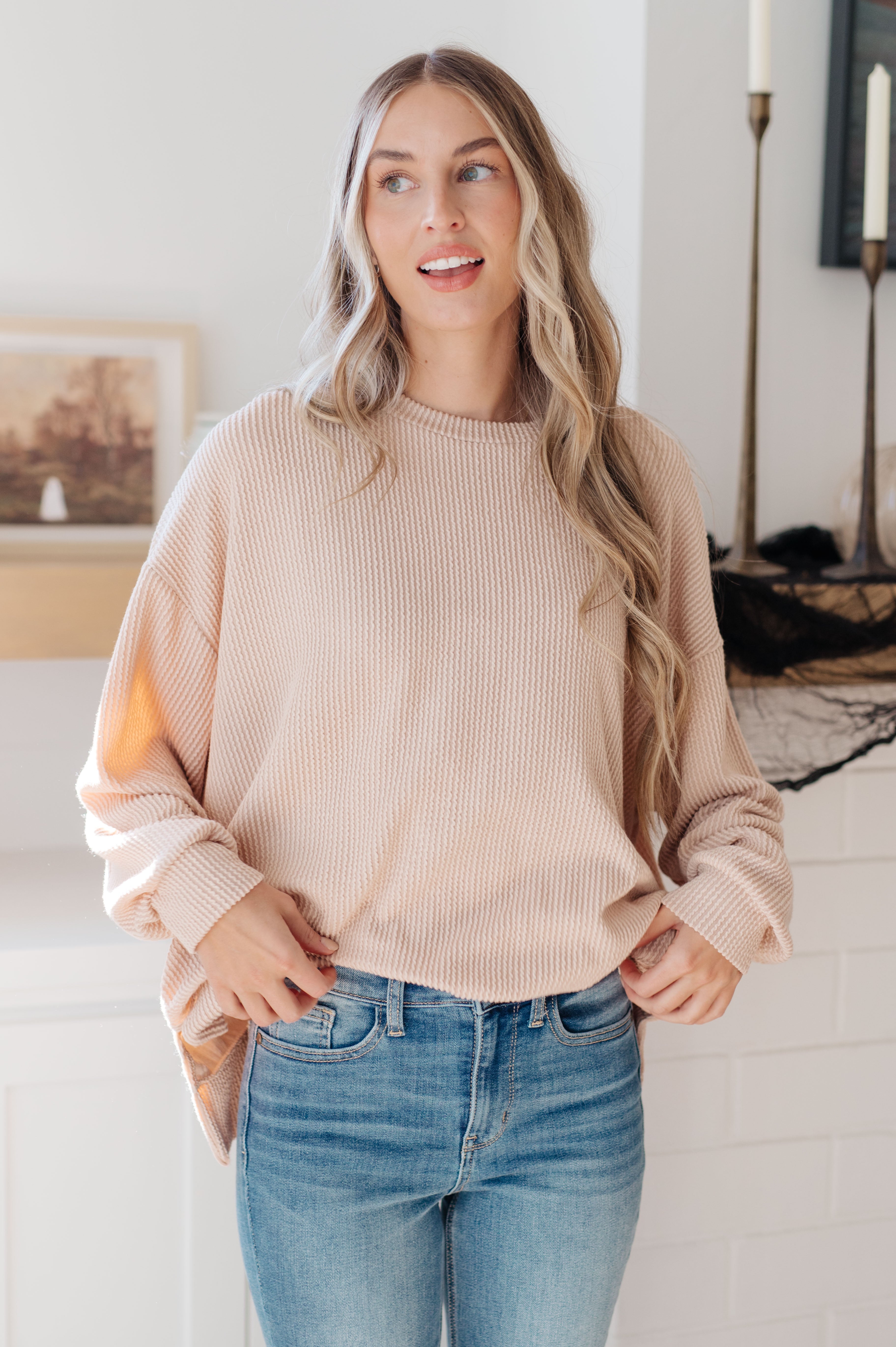 Woman wearing beige knitted pullover with relaxed fit paired with blue jeans indoors