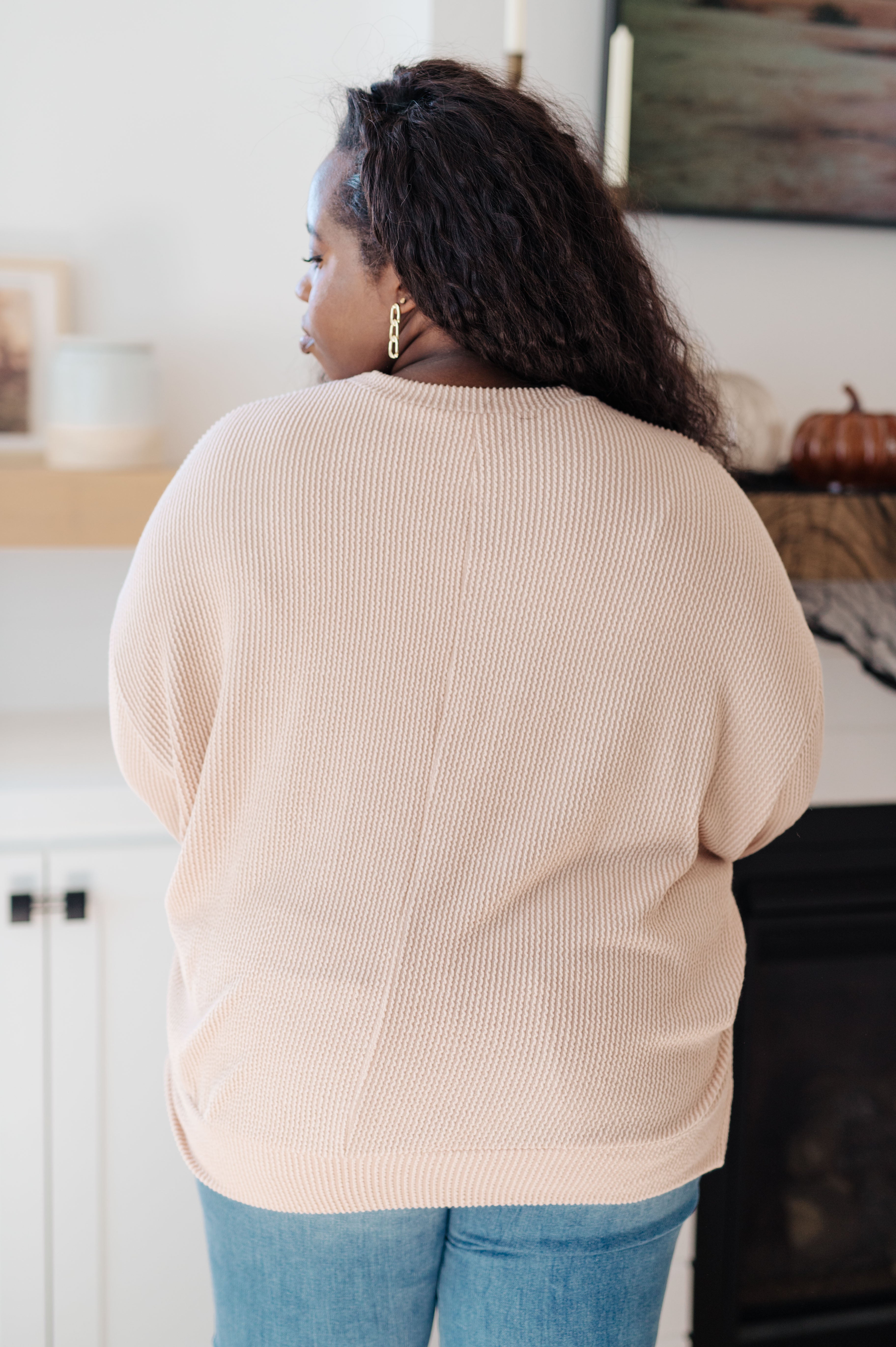 Curvy woman wearing a beige knit pullover with long sleeves and relaxed fit paired with blue jeans indoors