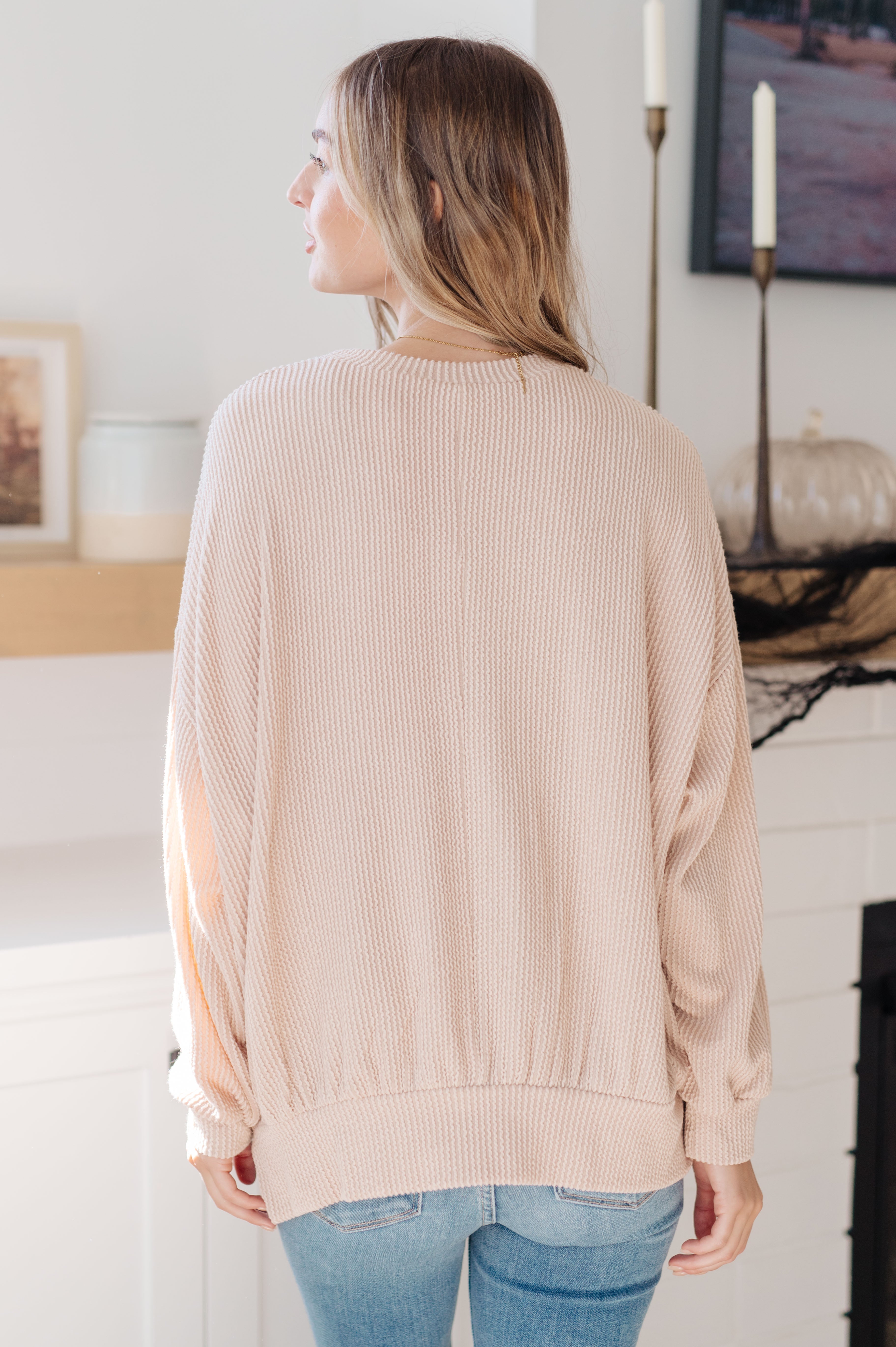 Woman wearing beige textured pullover with relaxed fit and ribbed cuffs paired with light blue jeans indoors