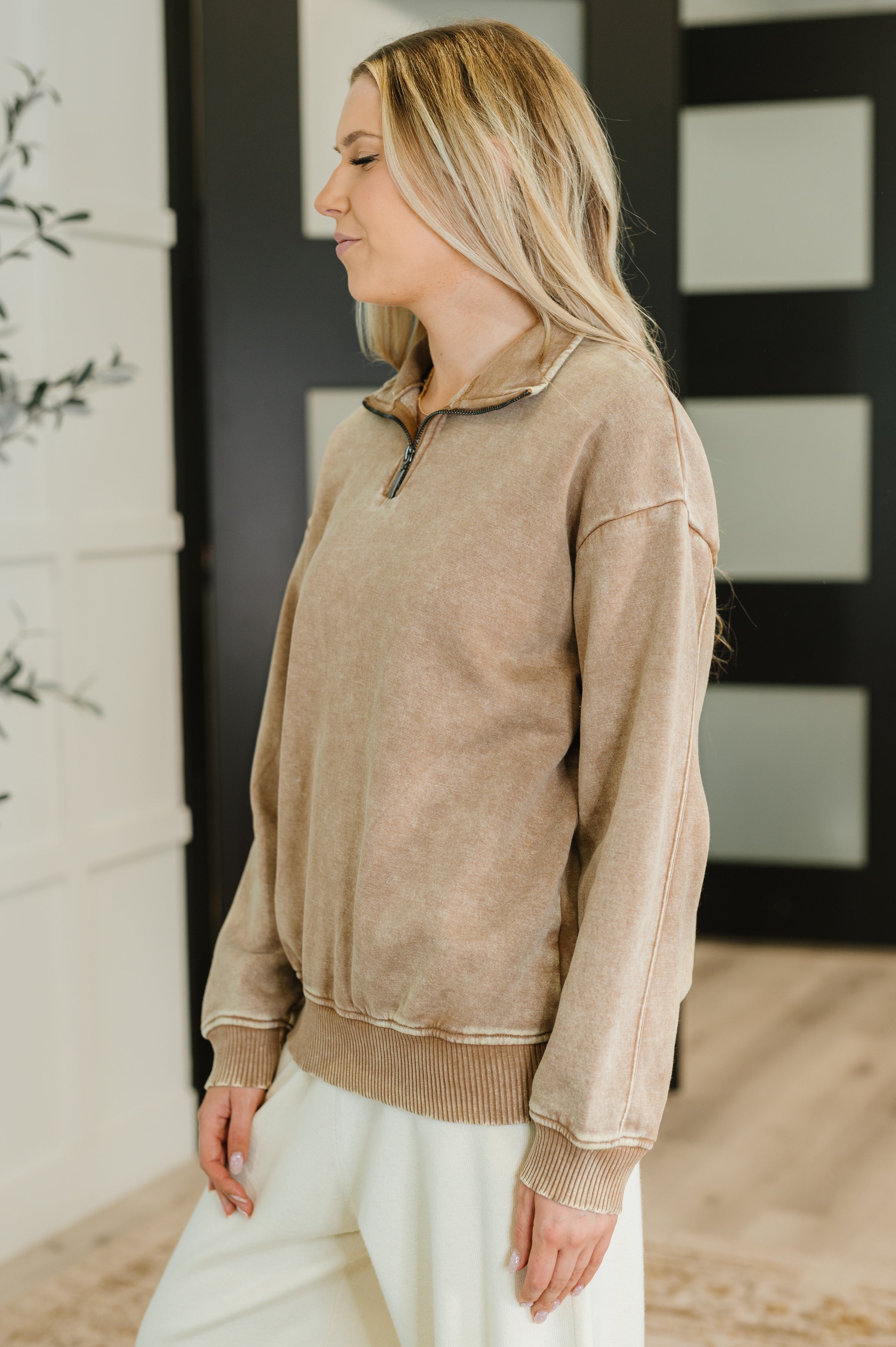 Woman wearing camel-colored half zip pullover with relaxed fit and ribbed cuffs standing indoors near black door