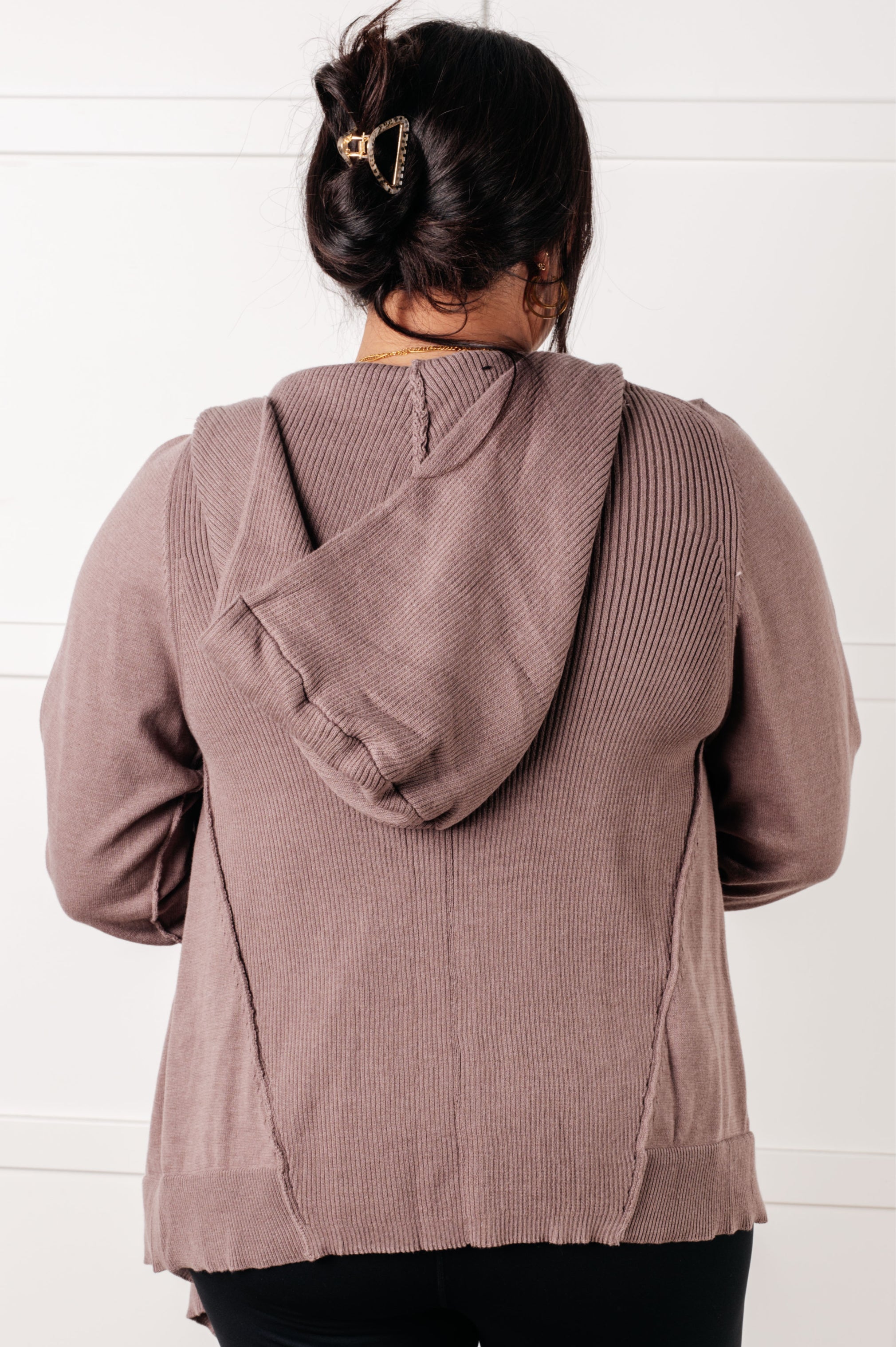 Back view of a mocha-colored plush cardigan with a hood worn by a woman with dark hair and gold hair clip