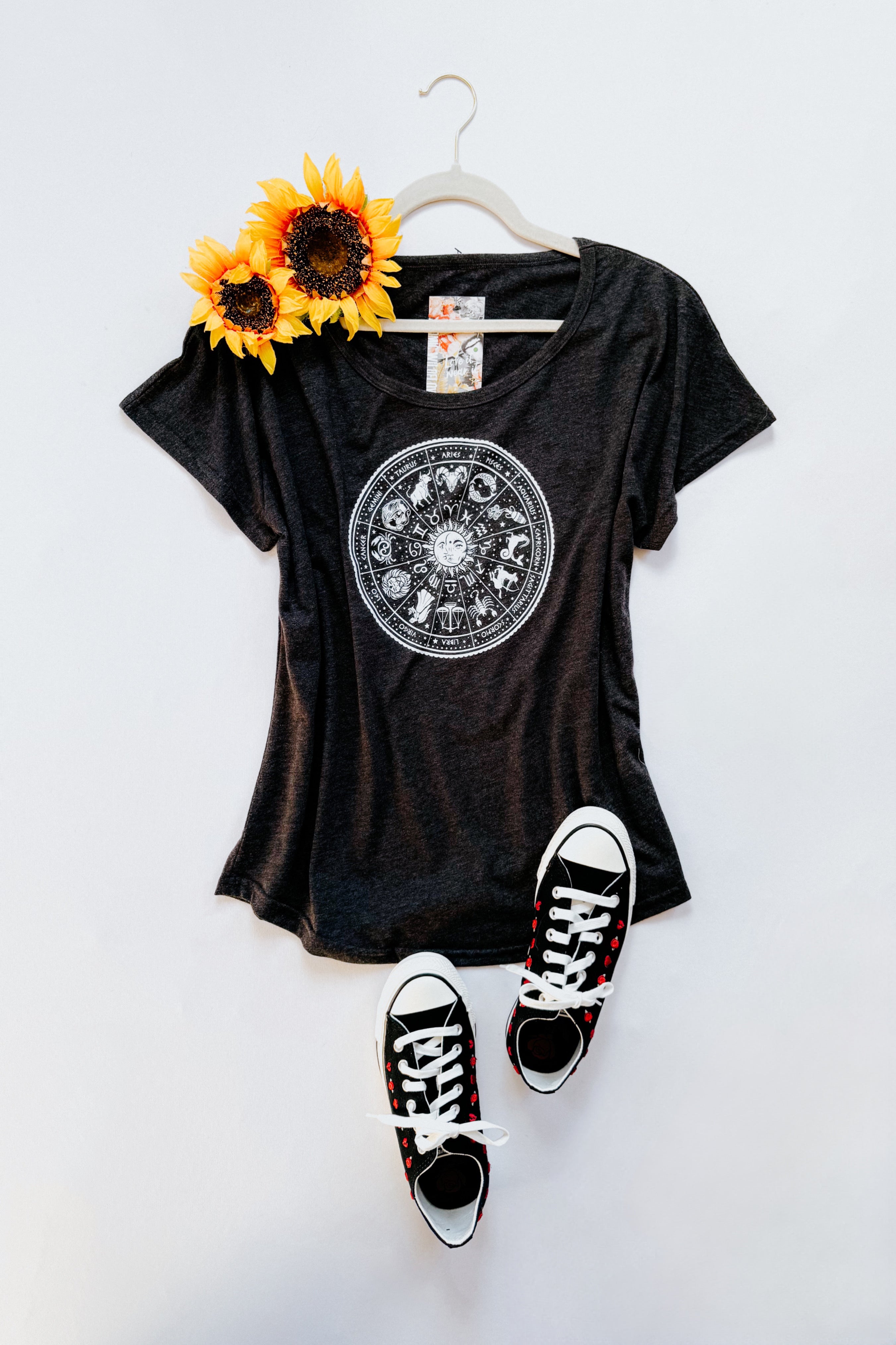 Charcoal slouchy top with zodiac circle design styled with black and white sneakers and sunflowers on hanger