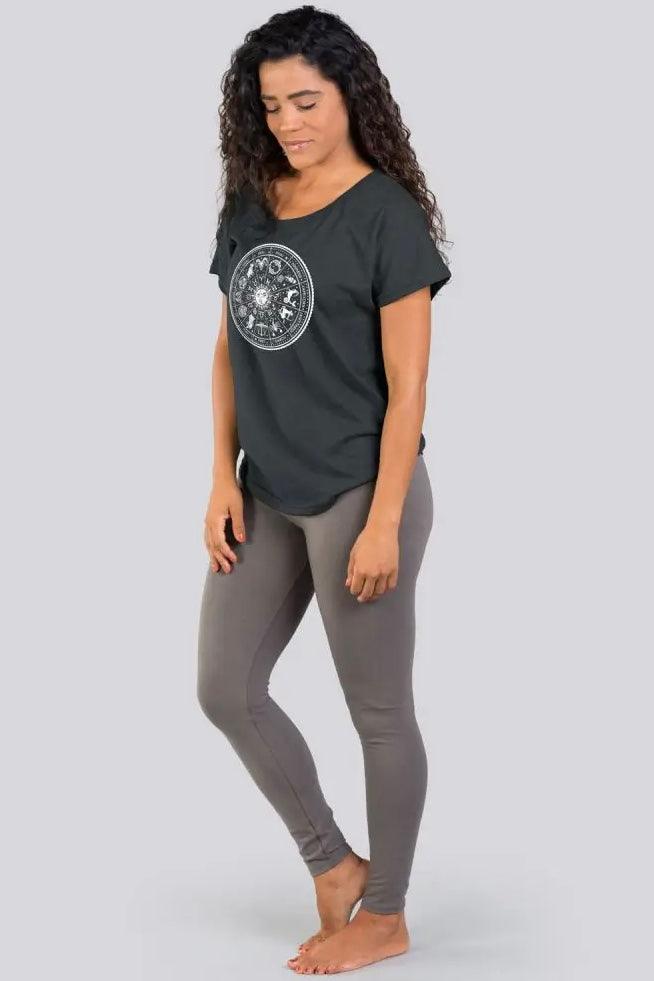 Woman wearing charcoal slouchy top with zodiac design paired with fitted gray leggings standing barefoot