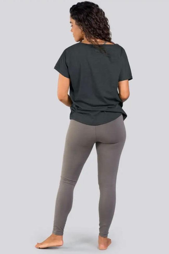 Woman with curly hair wearing charcoal slouchy top and taupe leggings standing barefoot against plain background