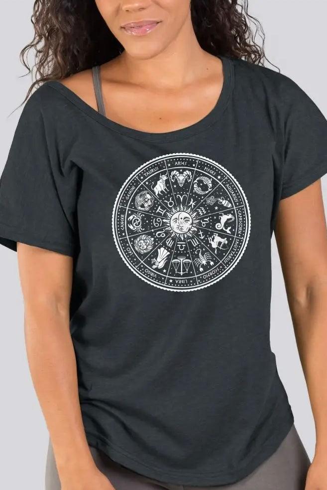Woman wearing charcoal slouchy top featuring white zodiac wheel graphic with casual straps visible underneath