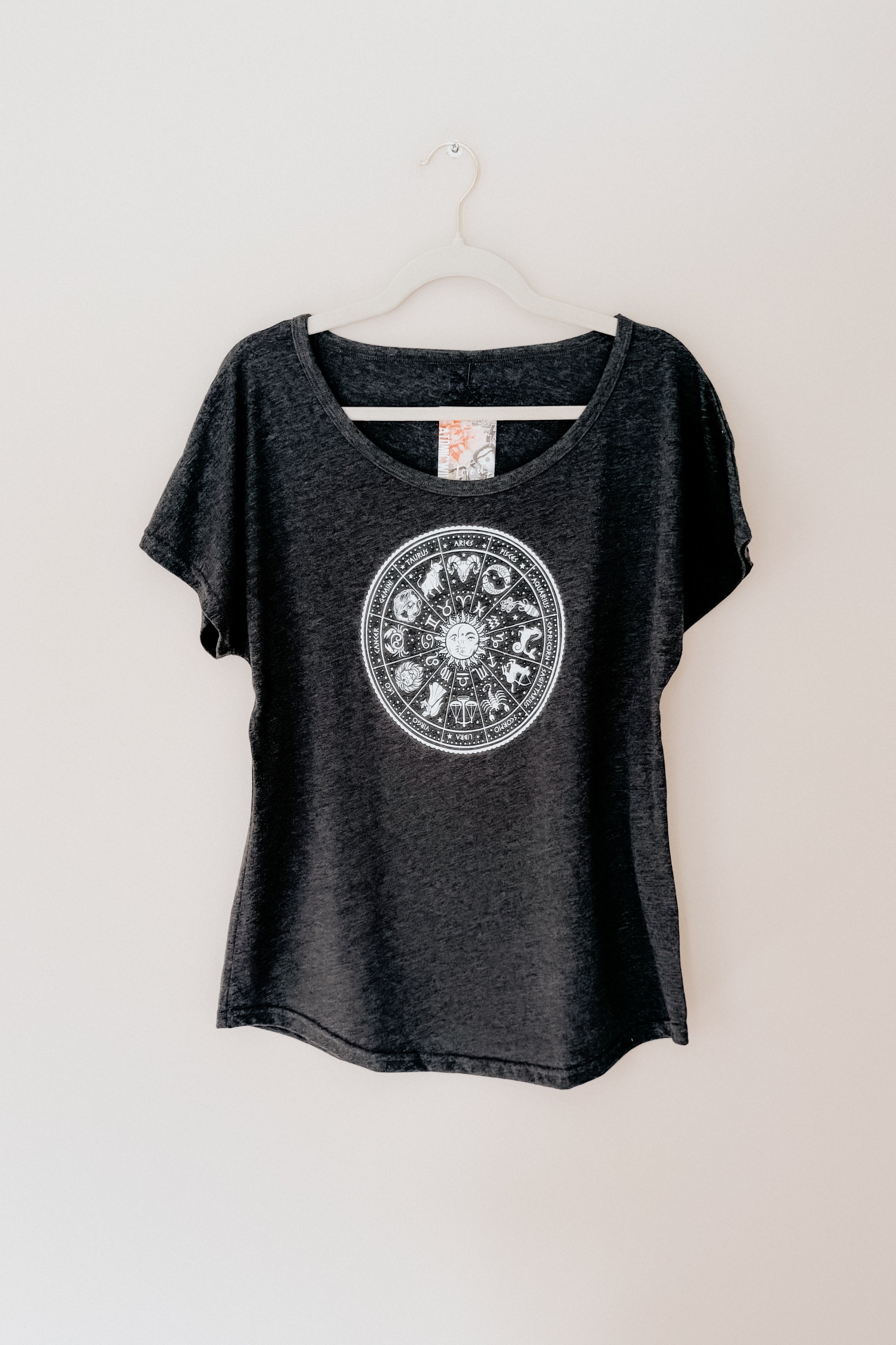 Charcoal slouchy top with white circular zodiac symbols printed on front hanging against light wall