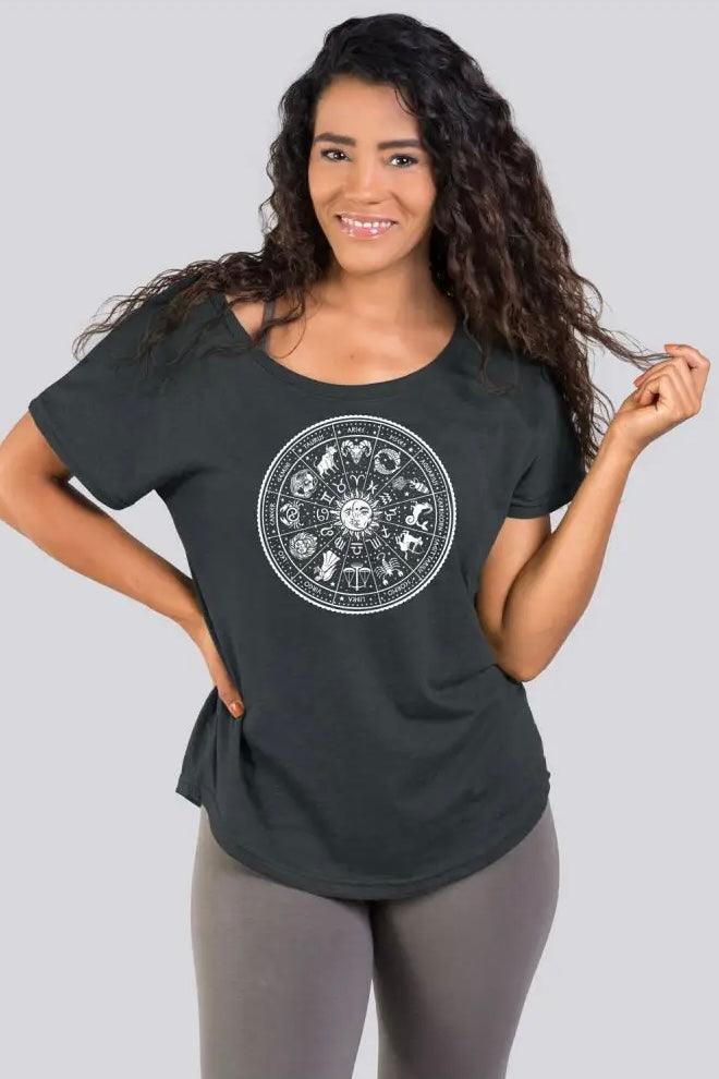 Woman wearing charcoal slouchy top with zodiac wheel graphic paired with neutral leggings posing against gray background