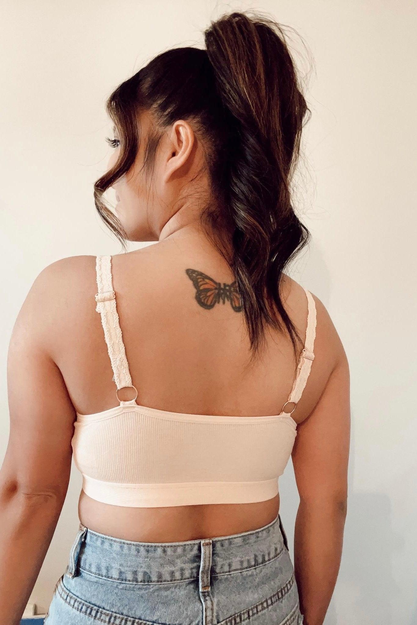 Back view of woman with butterfly tattoo wearing peach lace-trim bralette and high-waisted denim jeans