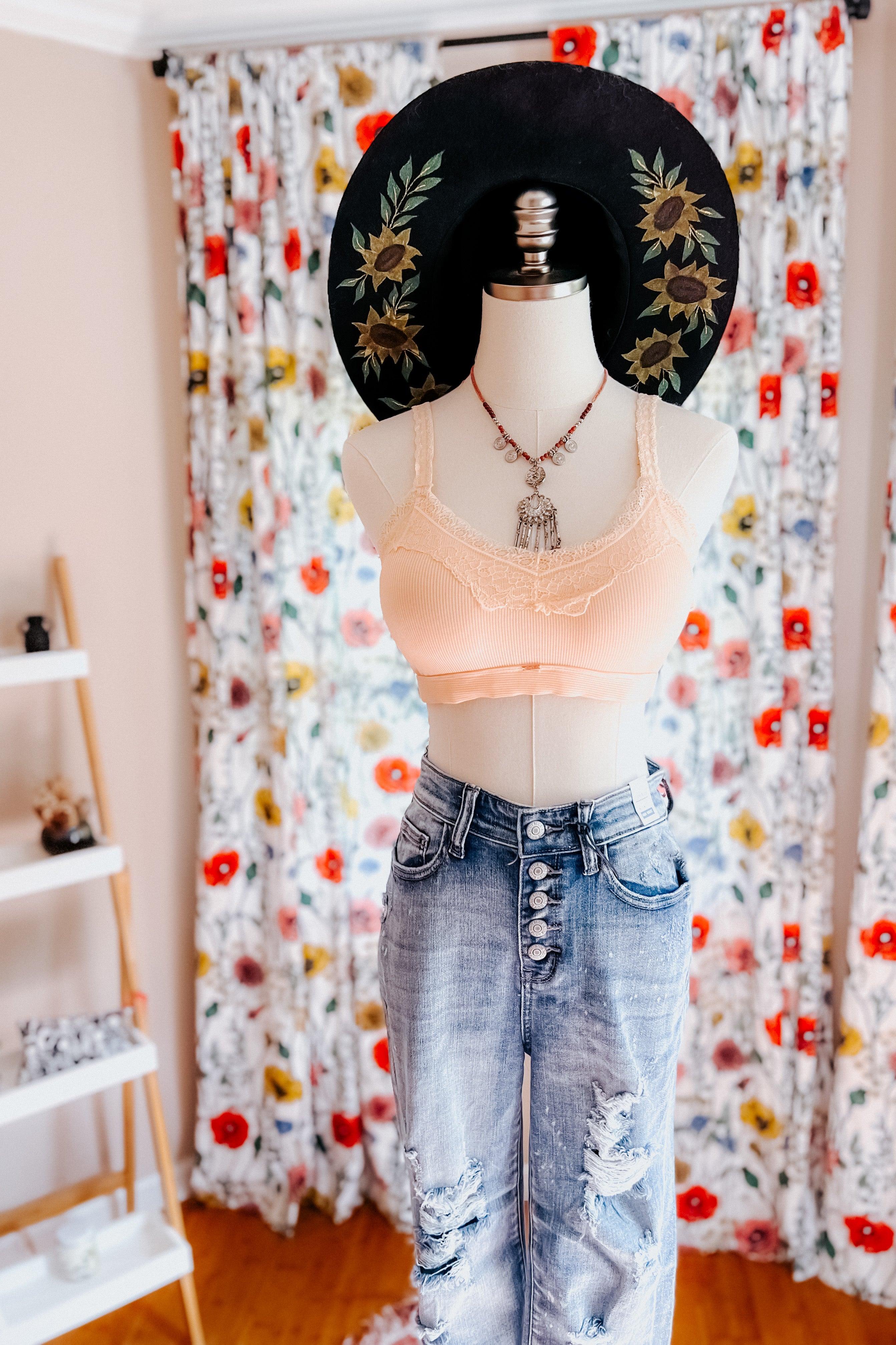 Mannequin wearing peach lace-trim bralette paired with distressed high-rise jeans and black floral wide-brim hat