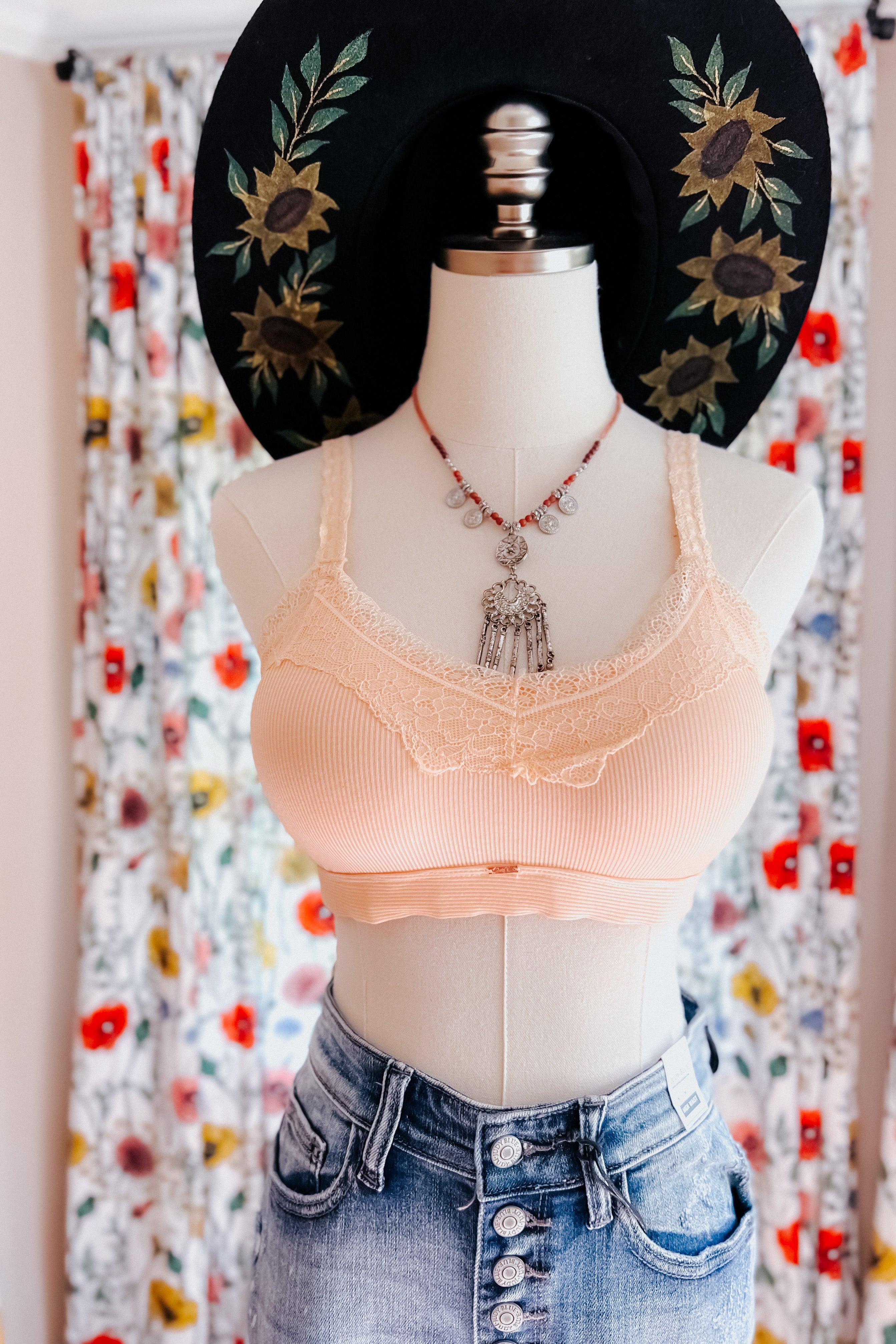 Mannequin wearing peach lace-trim bralette paired with high-waisted button-fly denim jeans and floral embroidered hat