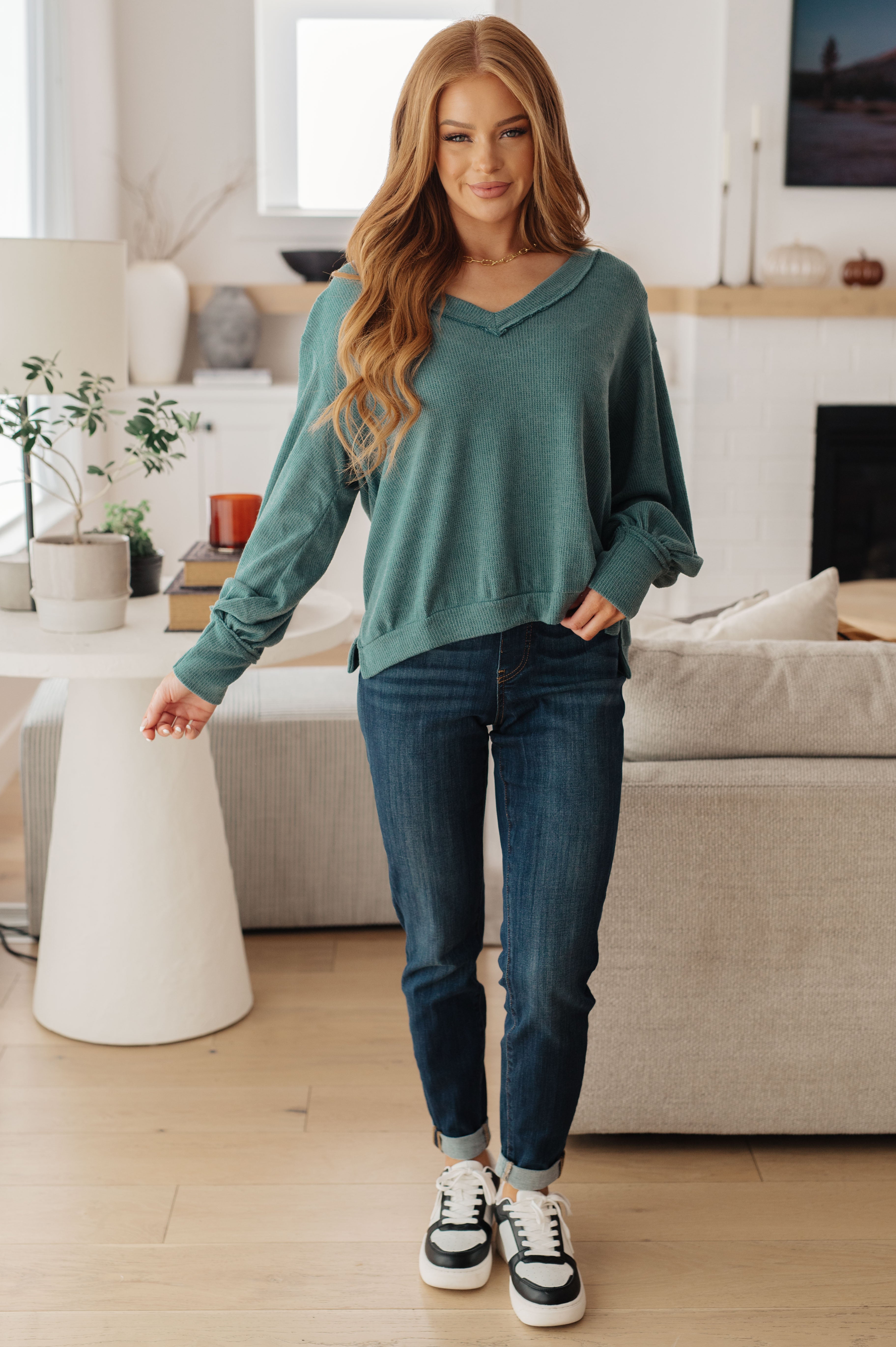 Woman wearing a teal sweater, blue jeans and sneakers in an indoor setting
