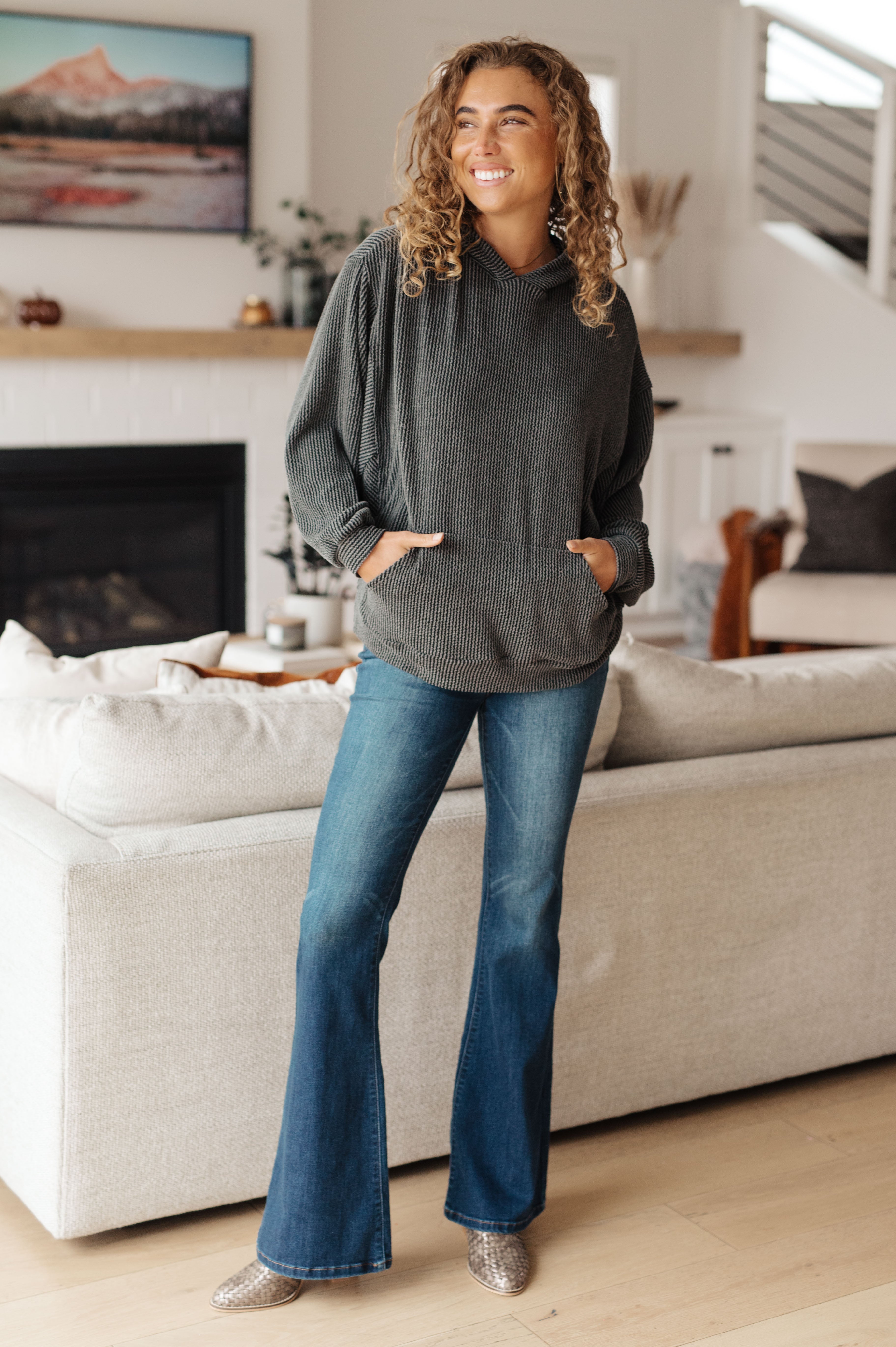 Woman wearing a grey rib knit hoodie over blue jeans and animal print boots against an indoor setting.