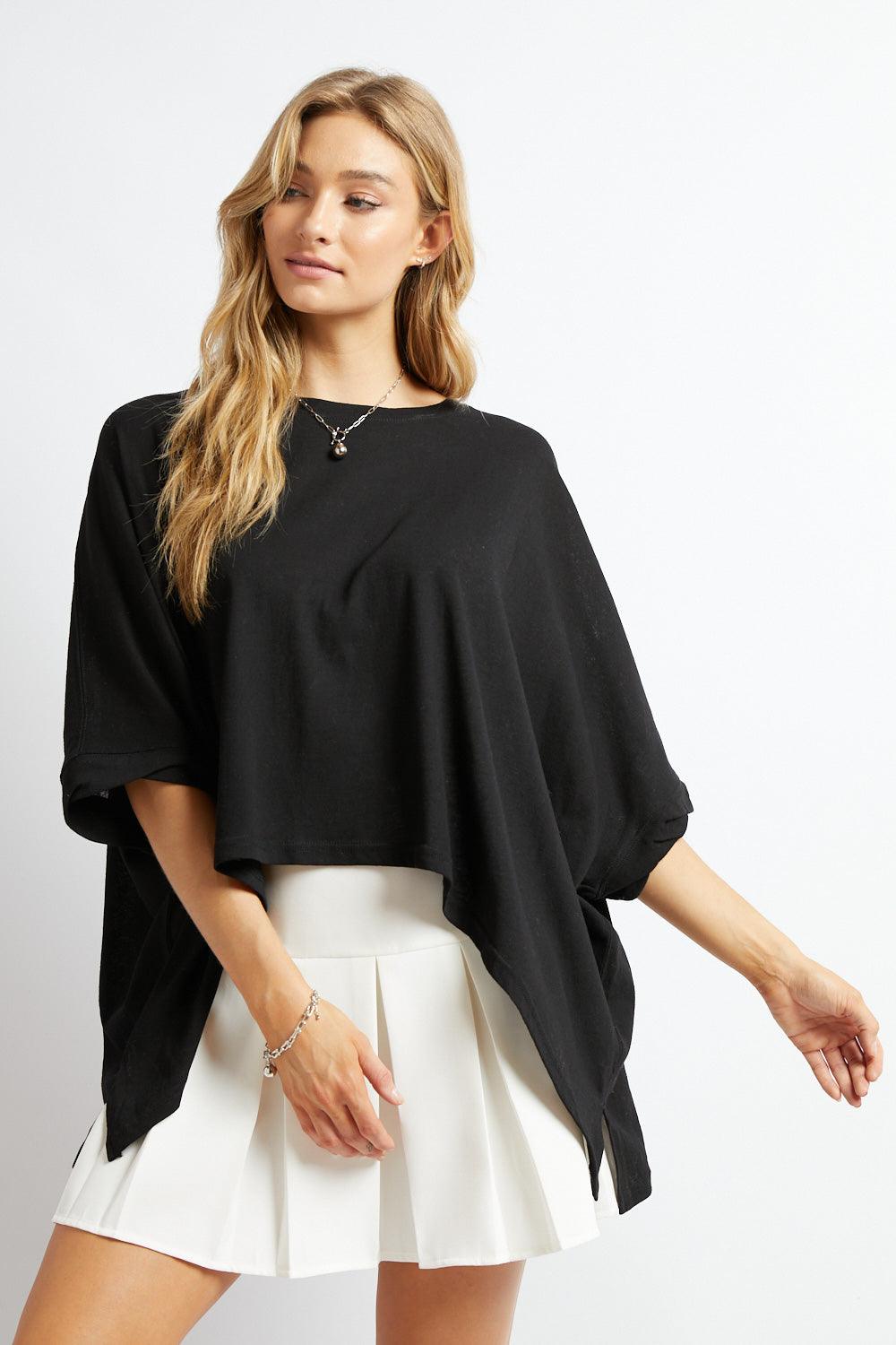 Woman wearing loose black All My Life Boxy Top with dropped sleeves paired with white pleated skirt against white background