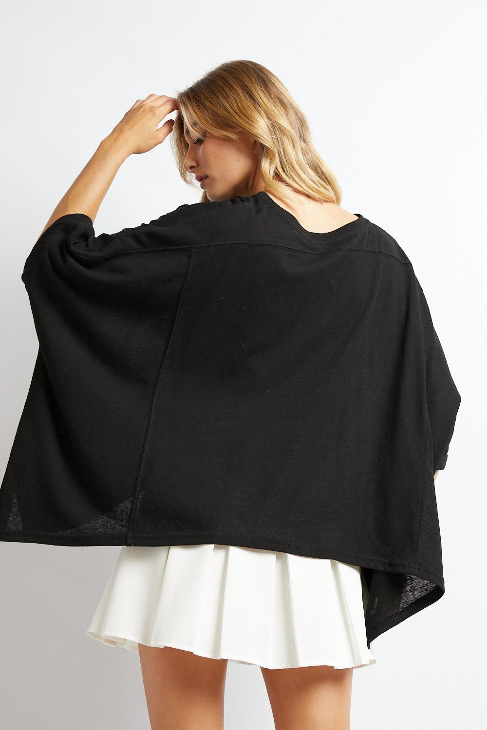 Back view of woman wearing black All My Life Boxy Top with wide sleeves and white pleated skirt against white background