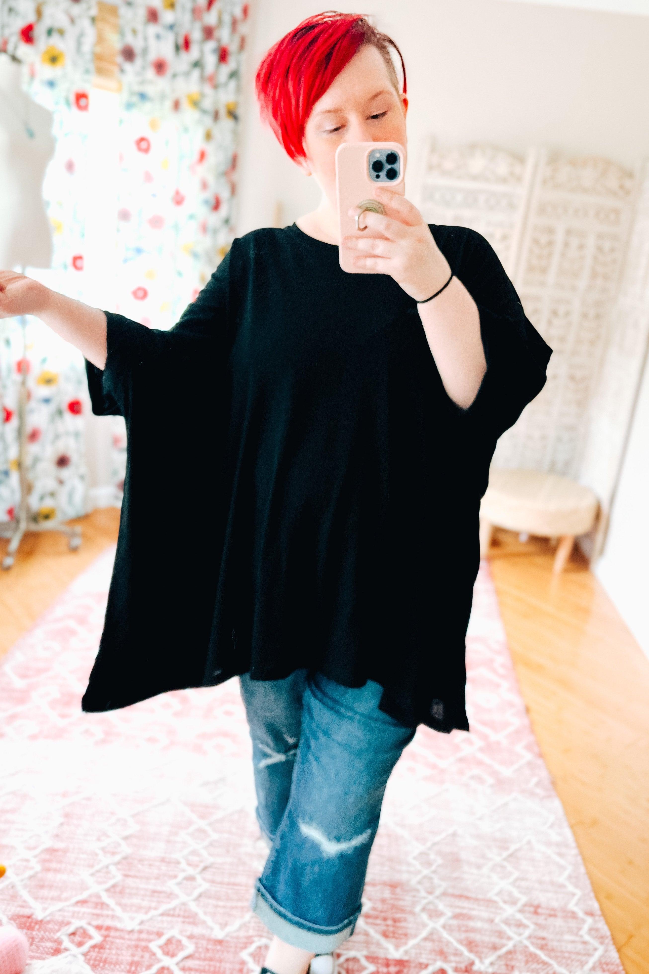 Woman with bright red hair wearing black All My Life Boxy Top with wide sleeves and cuffed jeans taking mirror selfie indoors