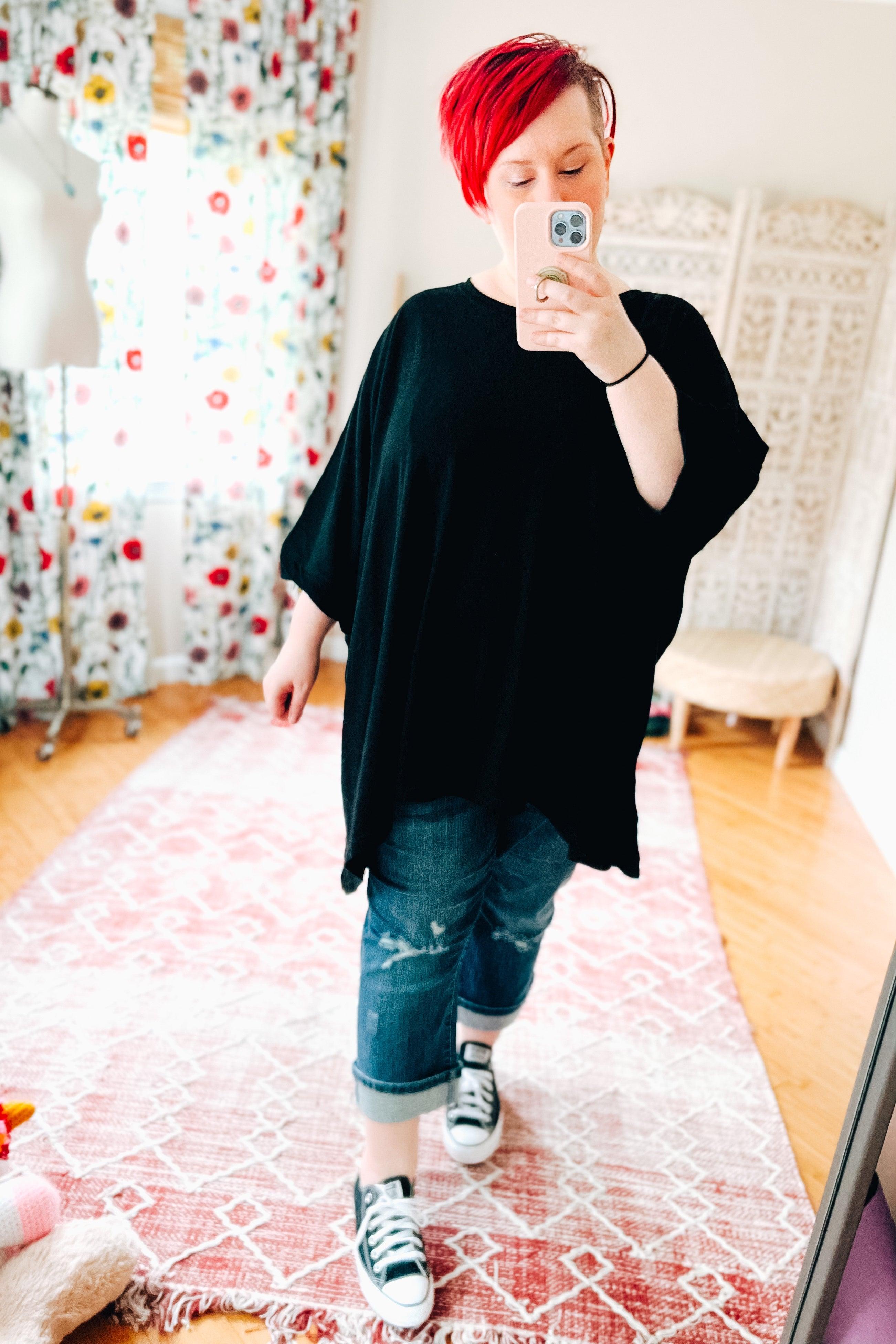 Woman with bright red hair wearing loose black All My Life Boxy Top standing on patterned rug taking mirror selfie